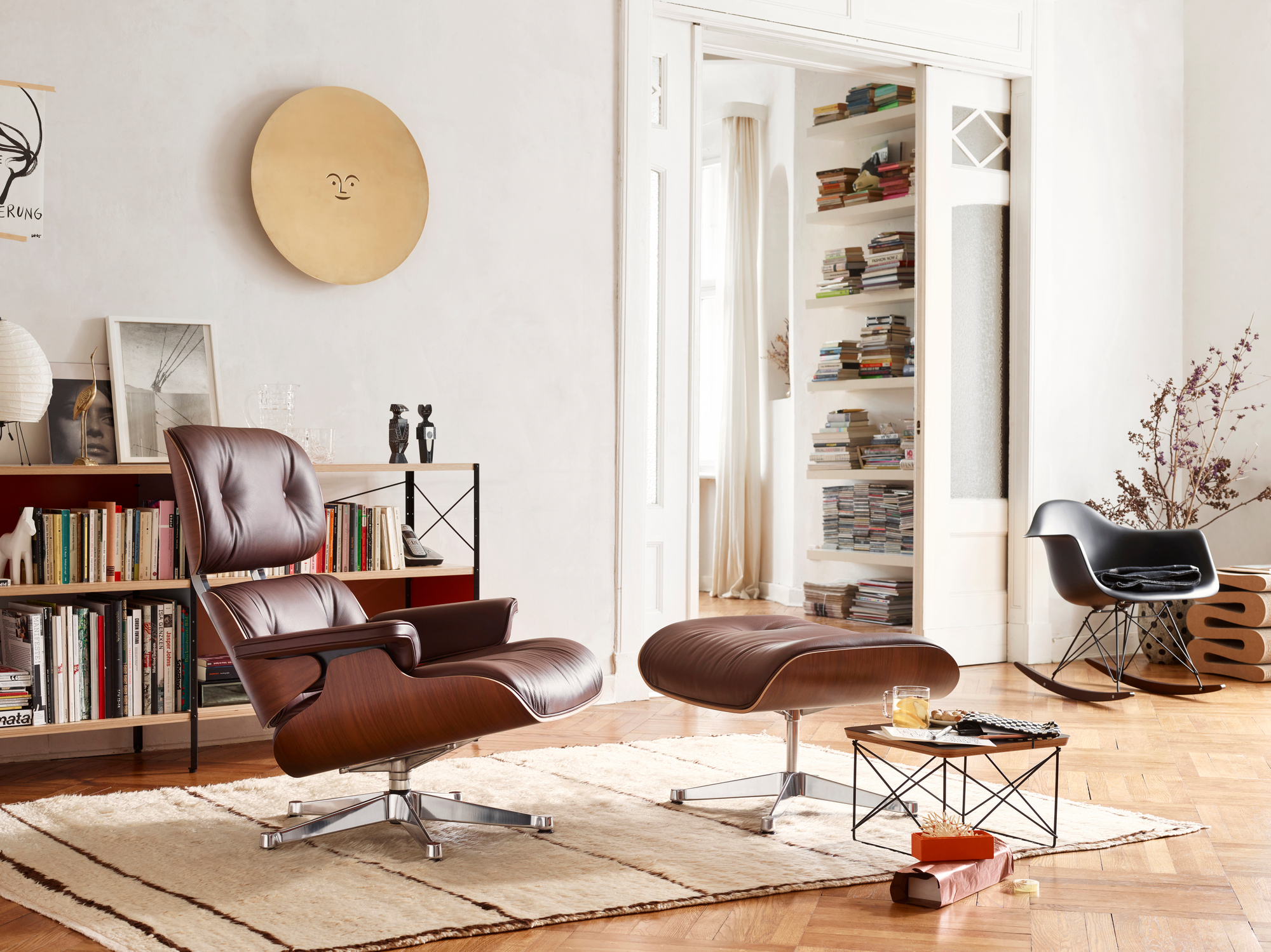Innenaufnahme mit braunem Ledersessel und Ottomane von Vitra, Bücherregal, Teppich und dekorativen Elementen für Wohnzimmer.