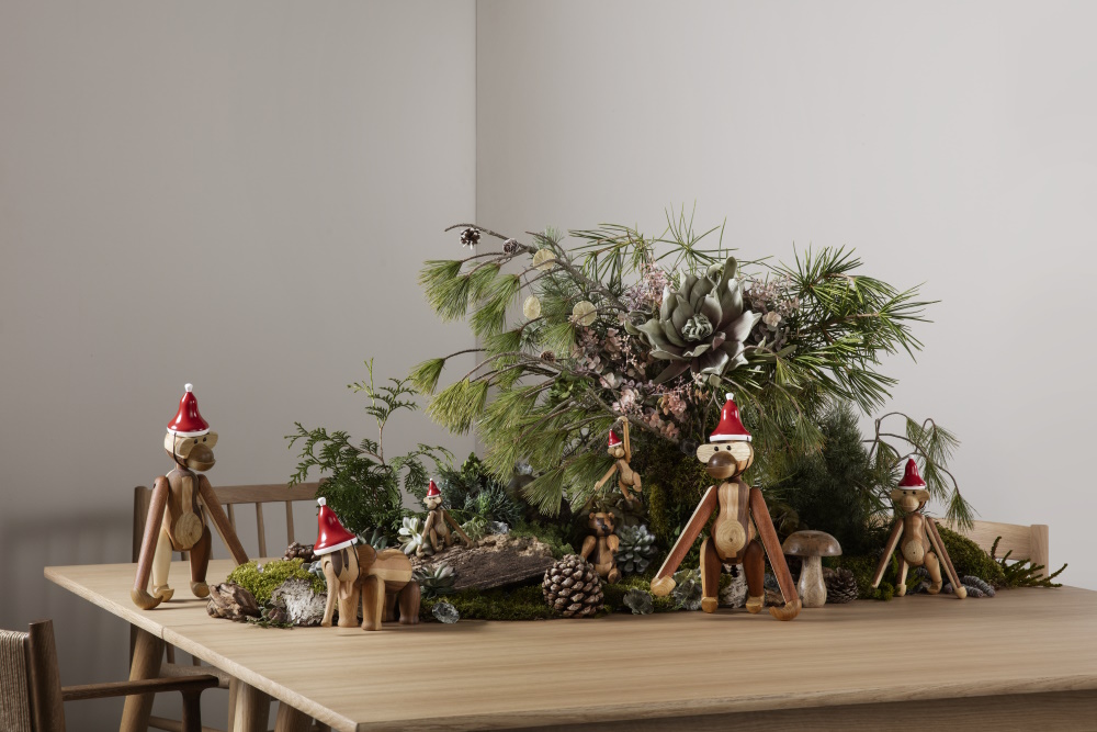 Holzfiguren mit Weihnachtsmützen als Tischdeko: Affen und Elefanten mit Tannenzweigen und Moos auf einem Holztisch.