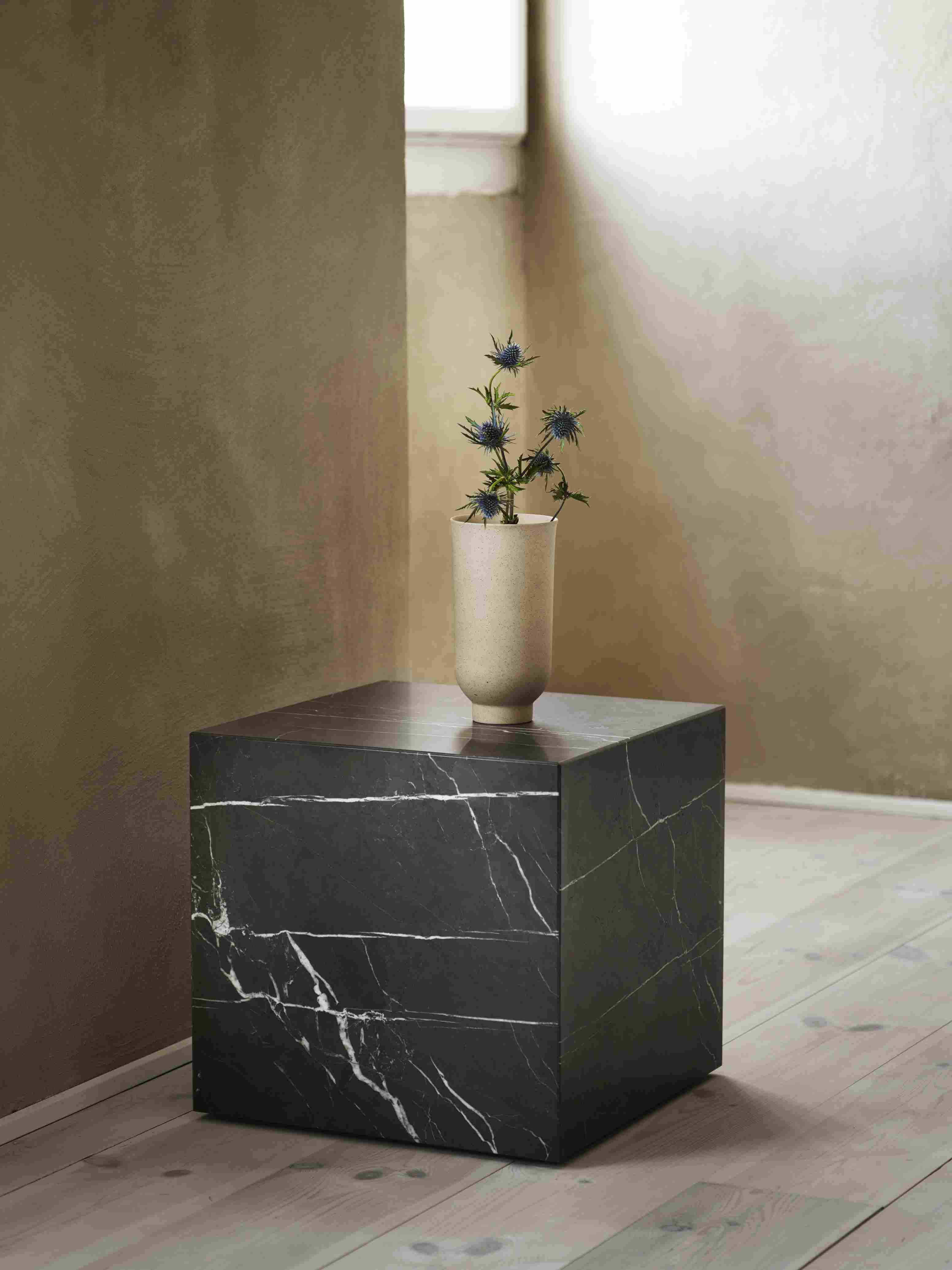 Audo Copenhagen Plinth Tisch aus schwarzem Marmor mit Vase und blauen Disteln.