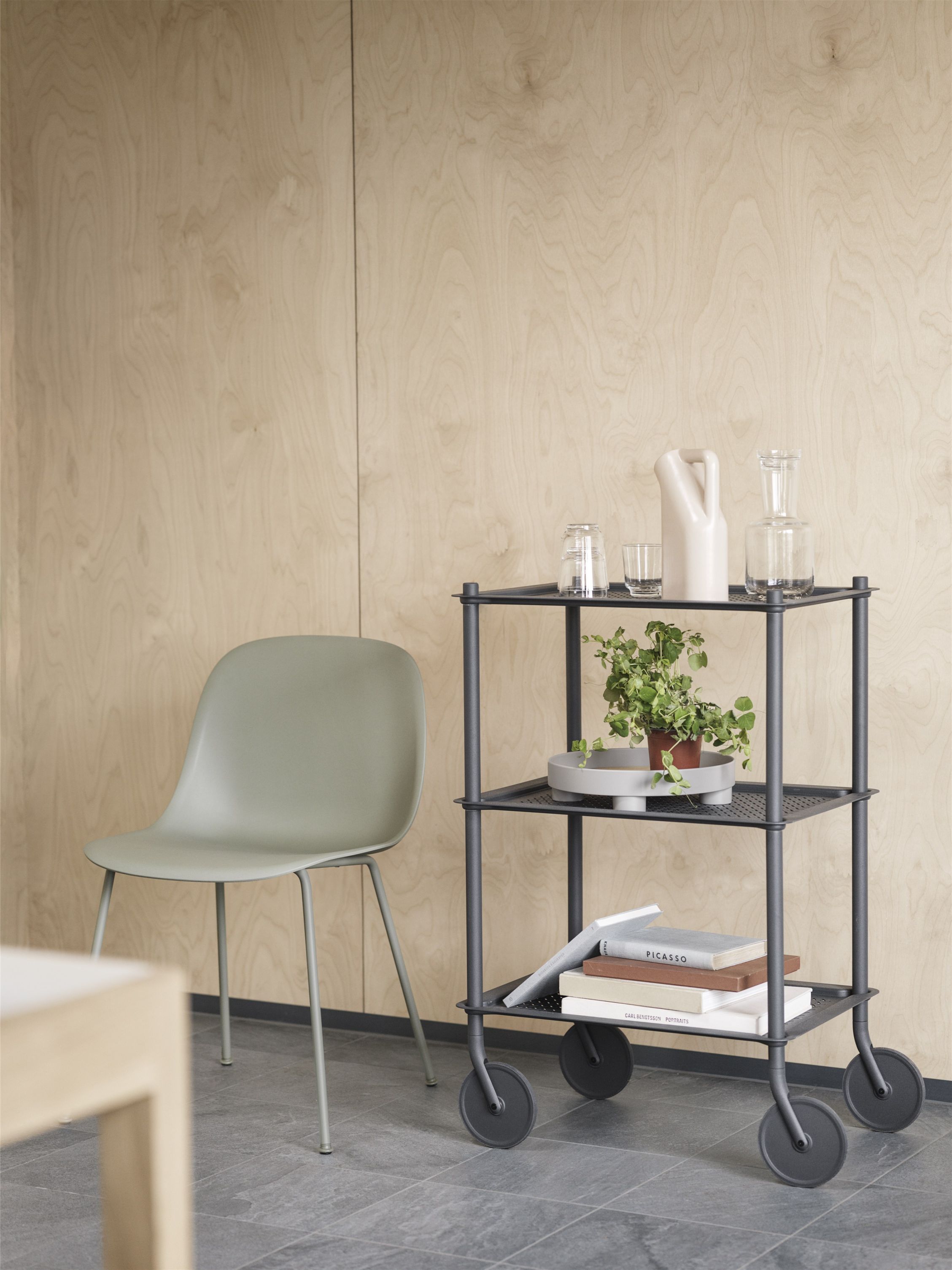 Heller, minimalistischer Raum mit Fiber Side Chair von Muuto und einem schwarzen Servierwagen mit Dekoration.