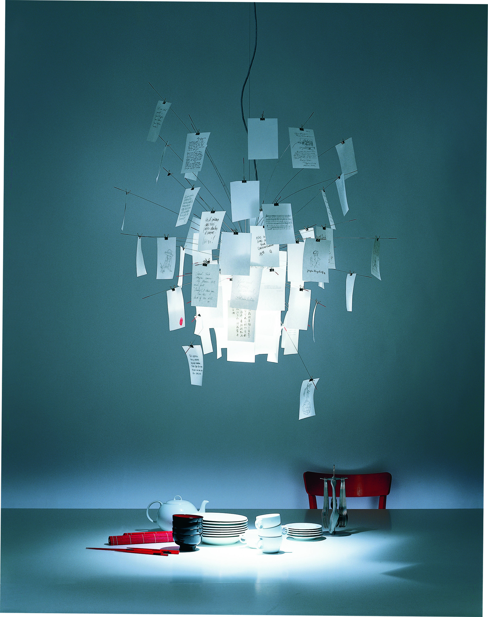 Zettel'z Hängeleuchte von Ingo Maurer über Esstisch mit Geschirr, moderne Designerlampe mit Notizen.