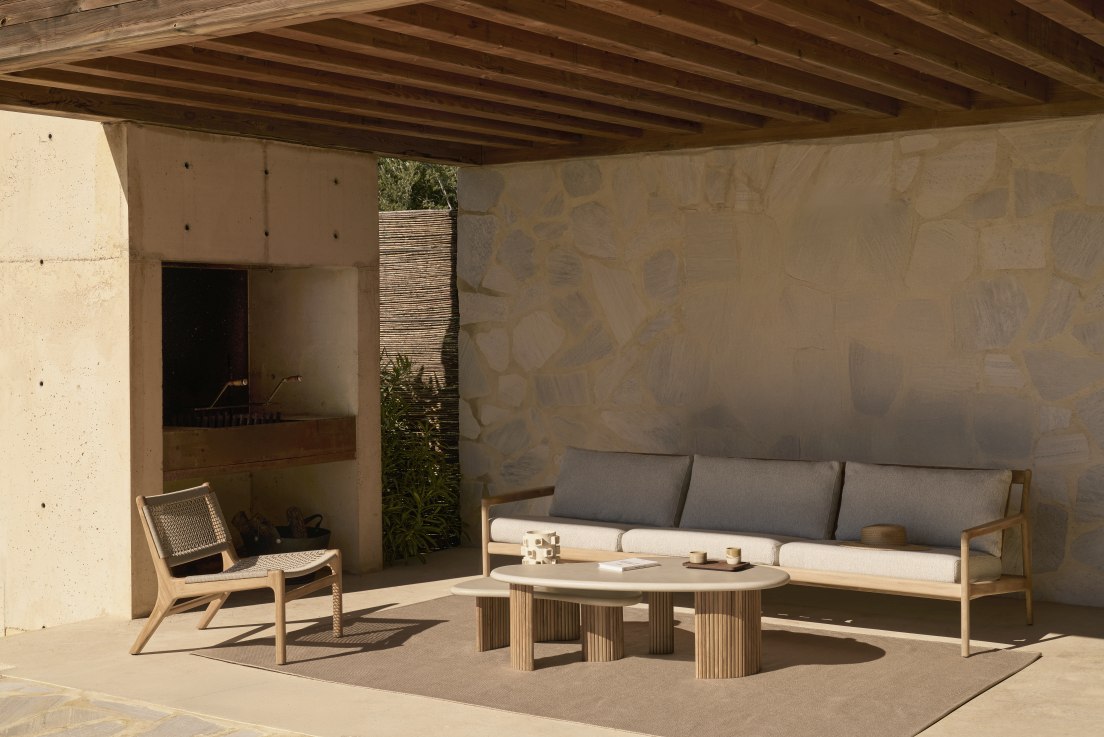 Ethnischraft Jack Loungesessel aus Teakholz mit beiger Kordel auf Terrasse mit Sofa und Tisch.