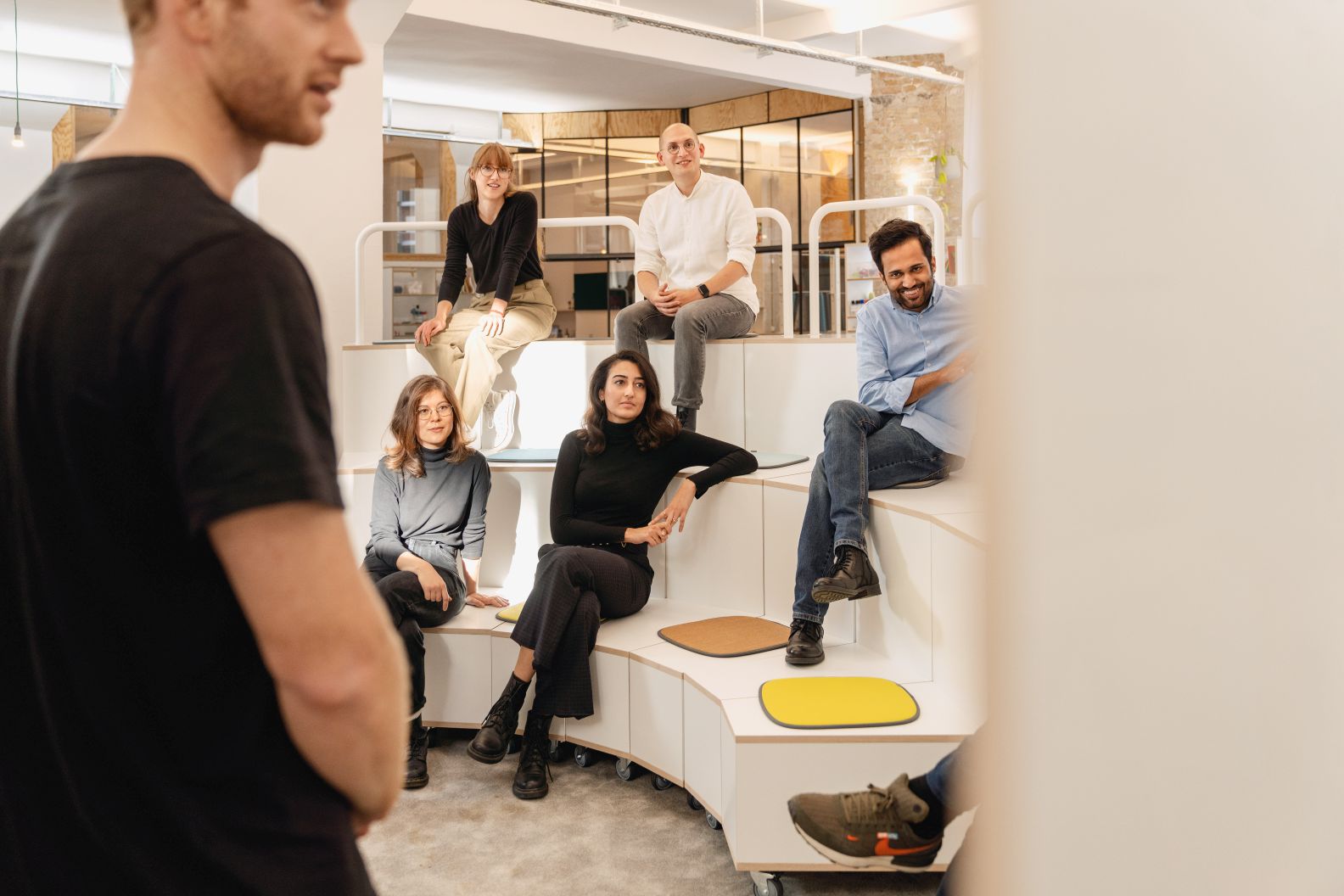 Gruppe junger Erwachsener sitzt auf What if We Fly Taskboard B Medienwand von Interstuhl im modernen Büro.