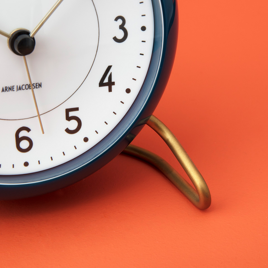 Detailaufnahme der Arne Jacobsen Station Tischuhr in Petrol-Weiss mit goldenem Standfuß. Designklassiker für Nachttisch und Schreibtisch.