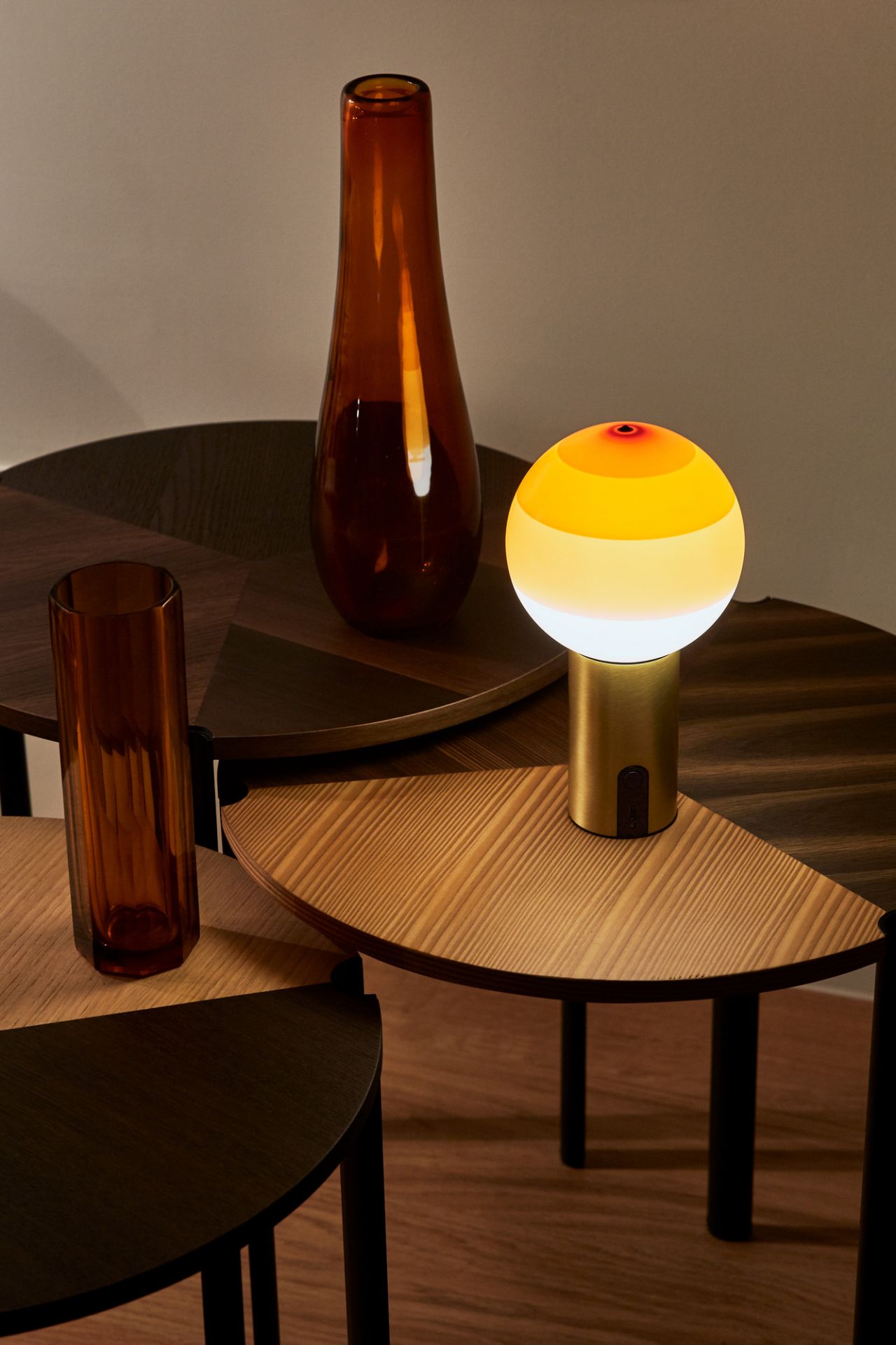 Gelbe Tischleuchte mit goldenem Sockel und Glasvasen auf modernen Beistelltischen aus Holz.