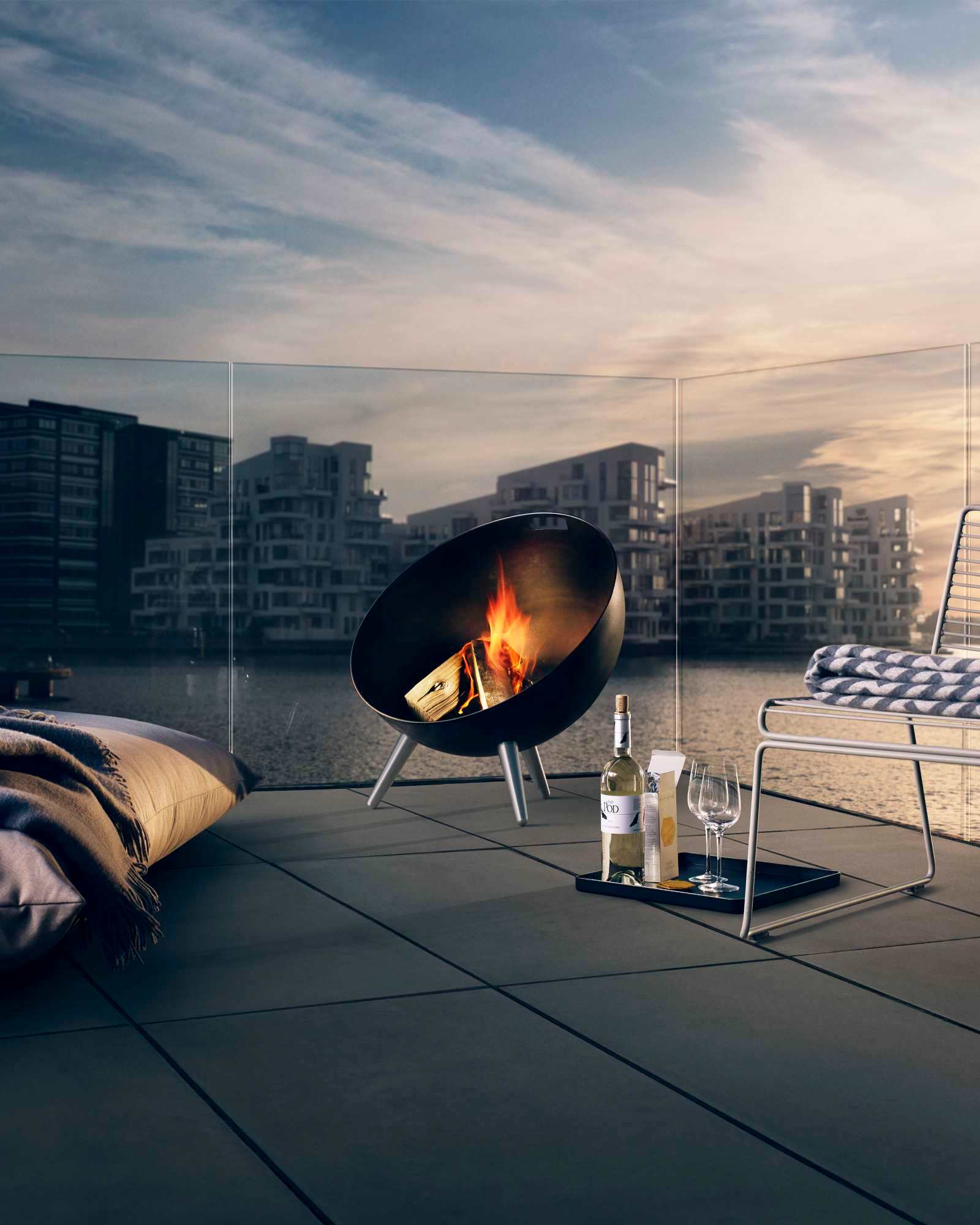 Fire Globe Feuerschale von Eva Solo mit brennendem Holz auf einer Terrasse am Wasser.