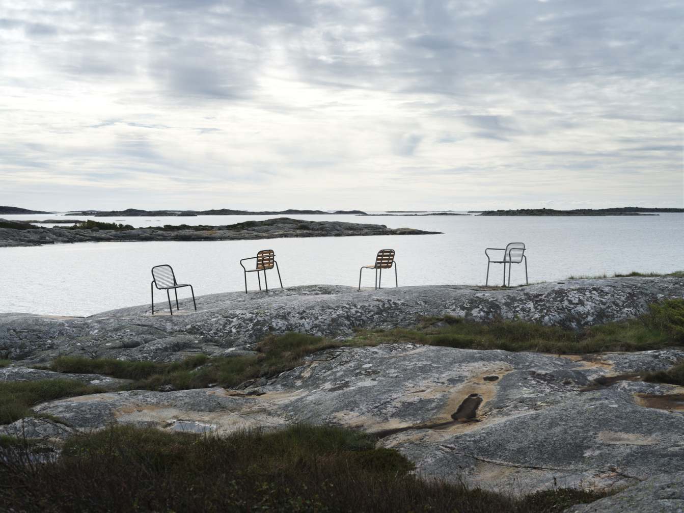 Vier Vig Chair Stühle von Normann Copenhagen im Outdoor-Bereich auf felsigem Untergrund mit Meerblick.