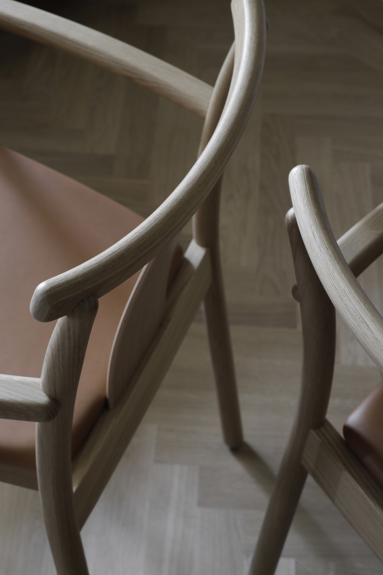 Detailaufnahme von zwei Merkur Dining Chair Stühlen mit Armlehnen von Audo Copenhagen, Holzgestell und Ledersitz.