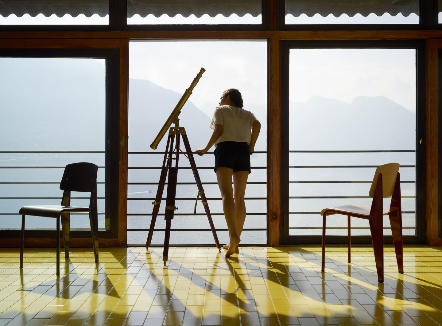 Vitra Standard Stuhl in Szene gesetzt mit Teleskop und Frau vor Panoramafenster mit Seeblick.