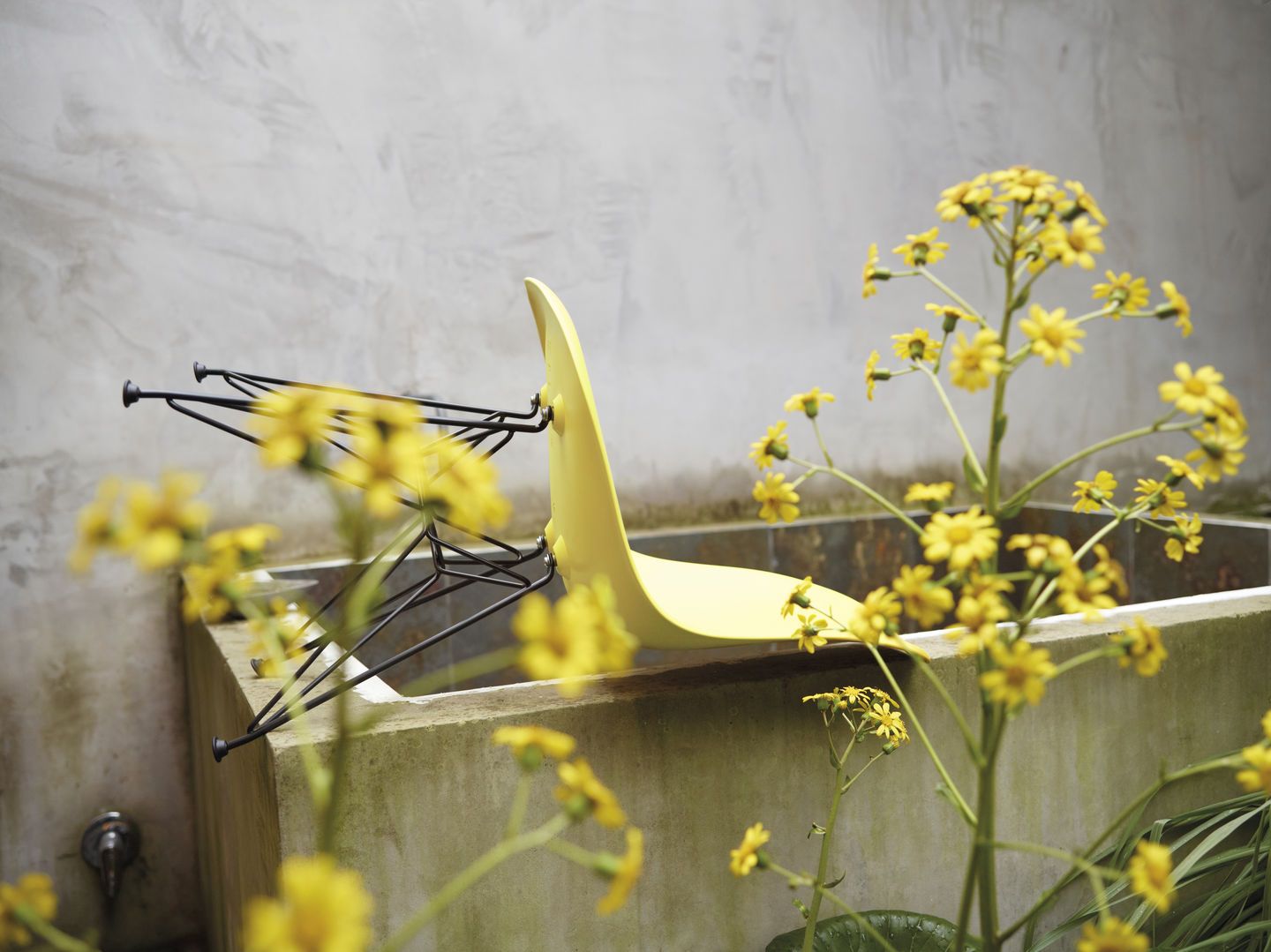 Gelber Eames Fiberglass Chair DSR Stuhl von Vitra, umgedreht, mit schwarzem Gestell und gelben Blumen.