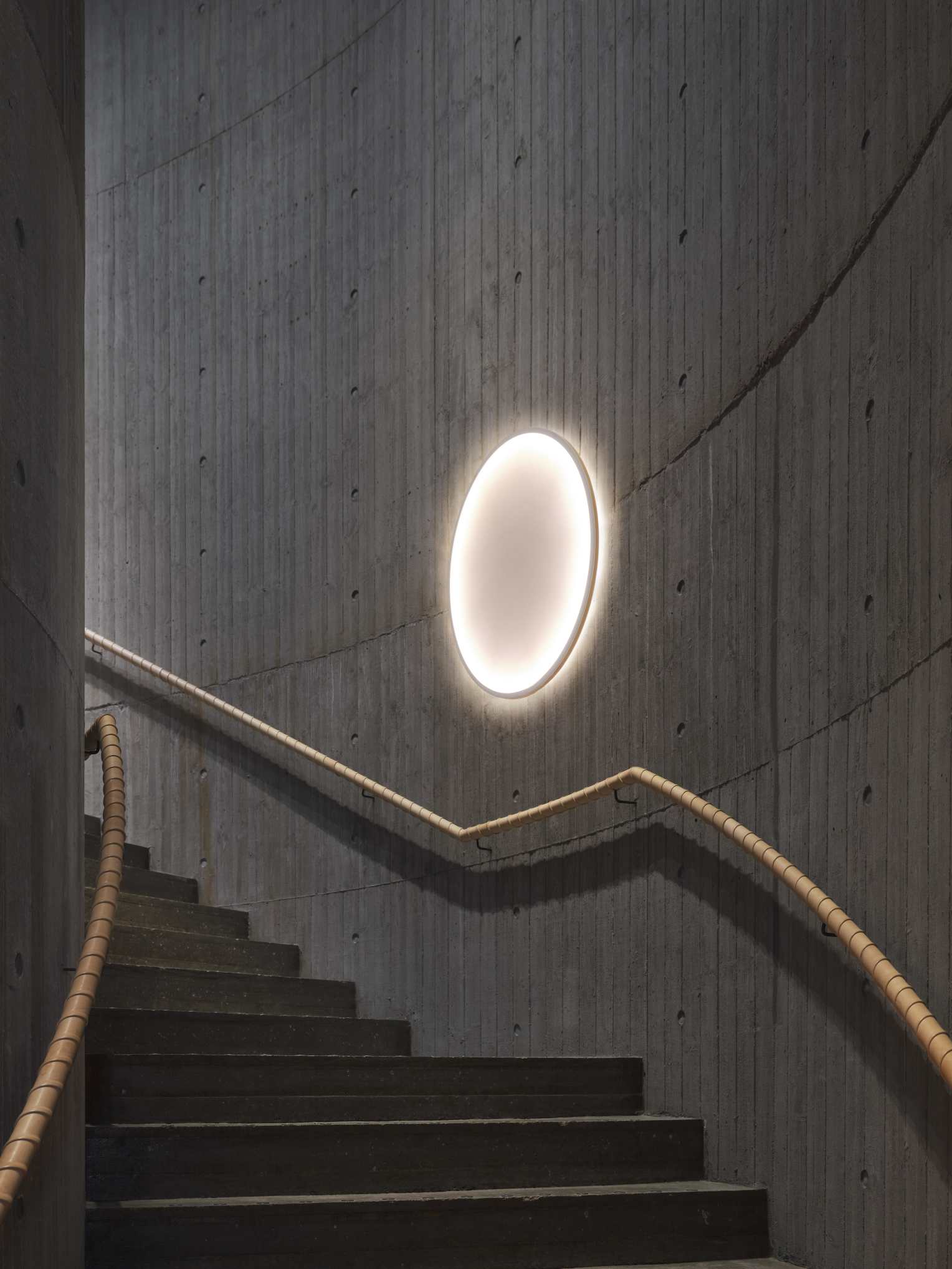 Ovale Calm Wall Lamp Wandleuchte von Muuto an einer Betonwand neben einer Treppe.