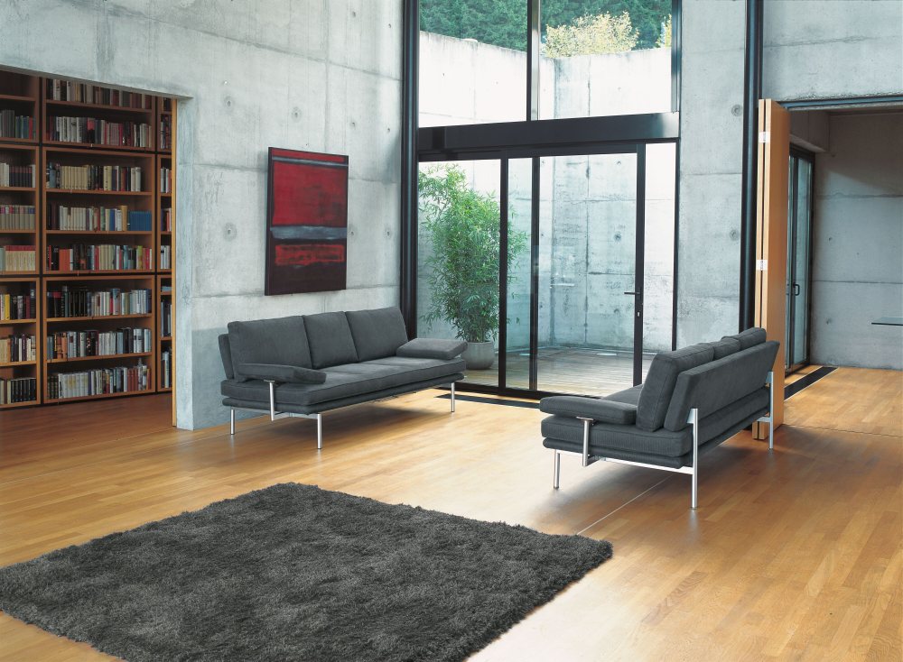 Graues Walter Knoll Sofa "Living Platform" mit Funktionsarmlehnen in modernem Wohnzimmer mit Teppich.