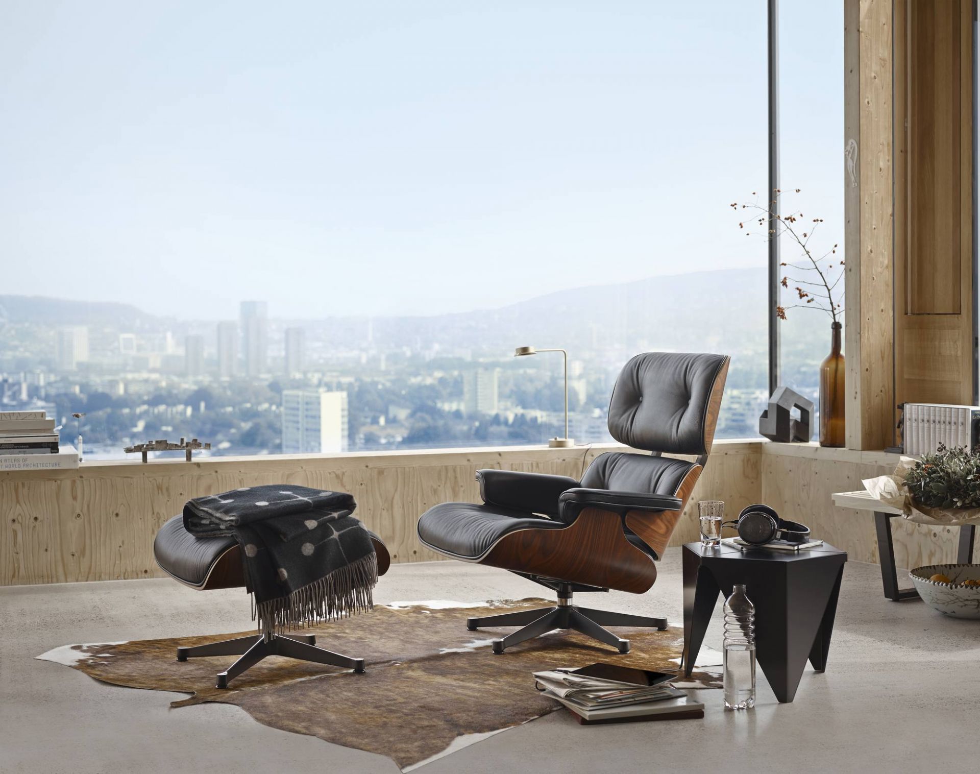 Eames Lounge Chair mit Ottoman in Premium Leder von Vitra vor Panoramafenster.