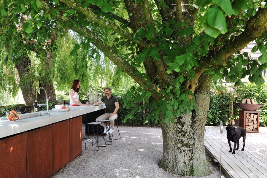 Extremis Tiki Hocker: Paar sitzt an Outdoor-Bar mit modernen Barhockern im Garten unter Baum.