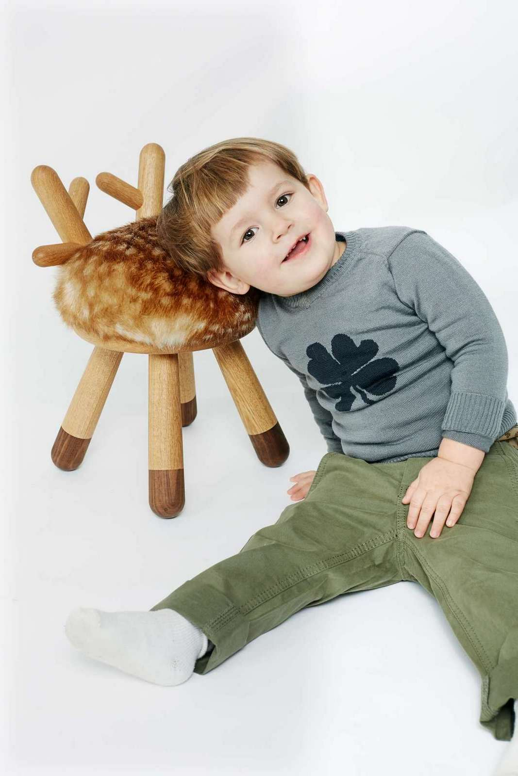 Kleiner Junge lehnt an Bambi Kinderstuhl von EO , ein Hocker mit Reh-Design und Holzbeinen.