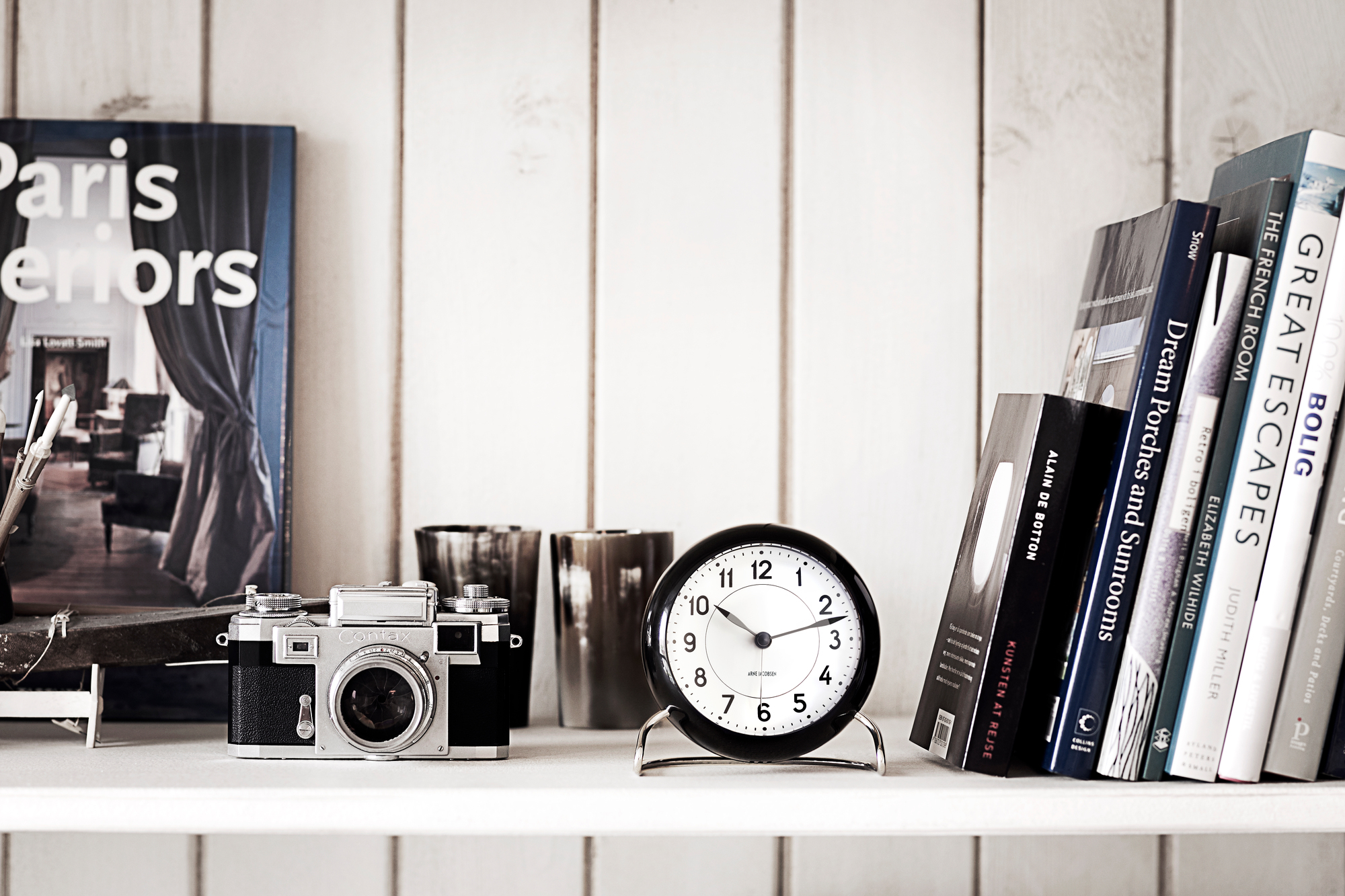 Arne Jacobsen Station Tischuhr Rosendahl Timepieces in Schwarz-Weiss auf Regal mit Büchern und Kamera.
