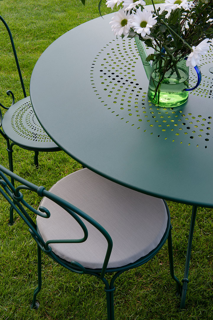 Grüner Fermob 1900 Gartentisch Ø 117 cm mit Stuhl und Blumenvase auf Rasen.