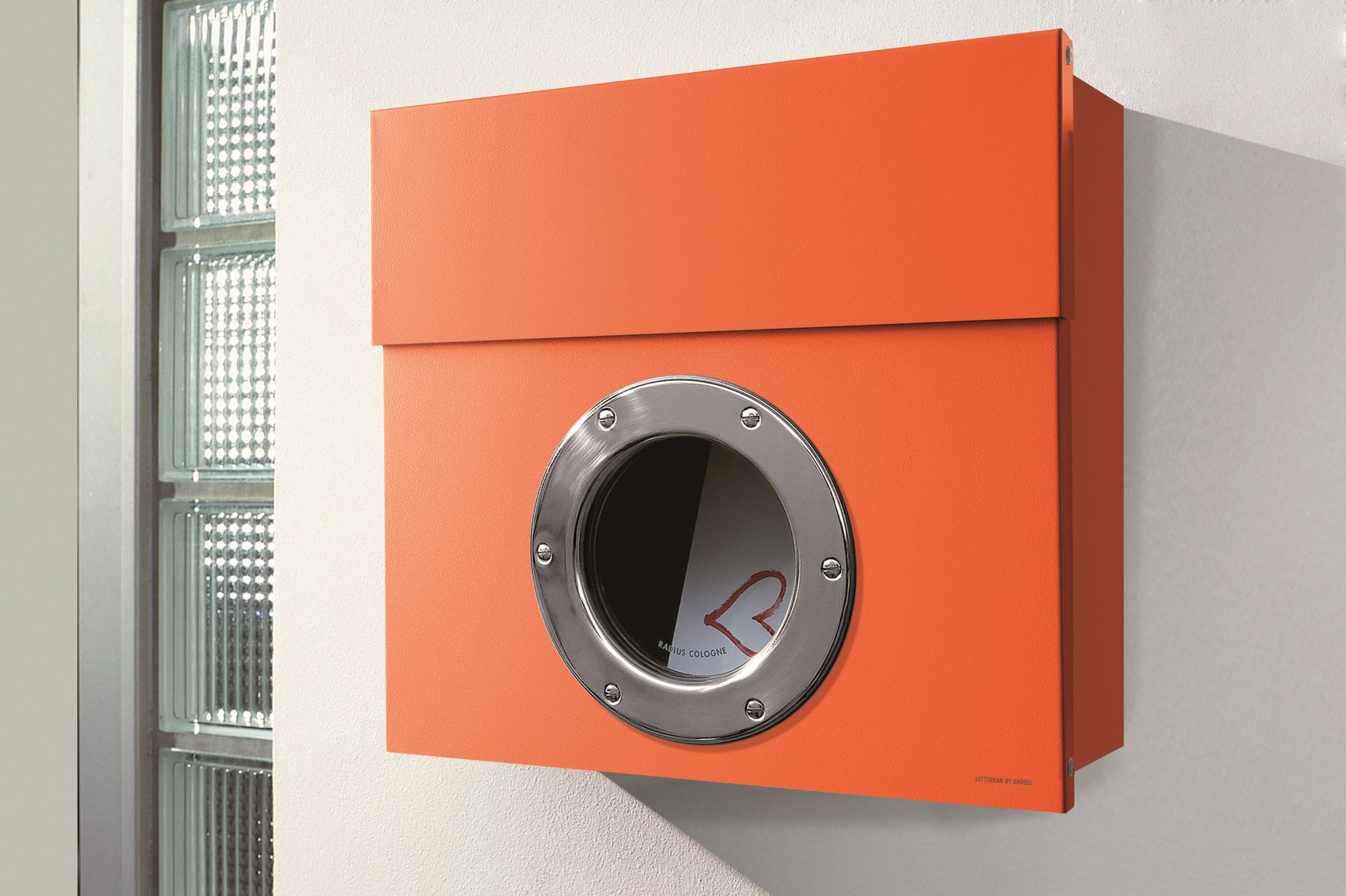 Orangefarbener Letterman Briefkasten mit Bullauge und Edelstahldetails an einer weißen Wand, modernes Design.