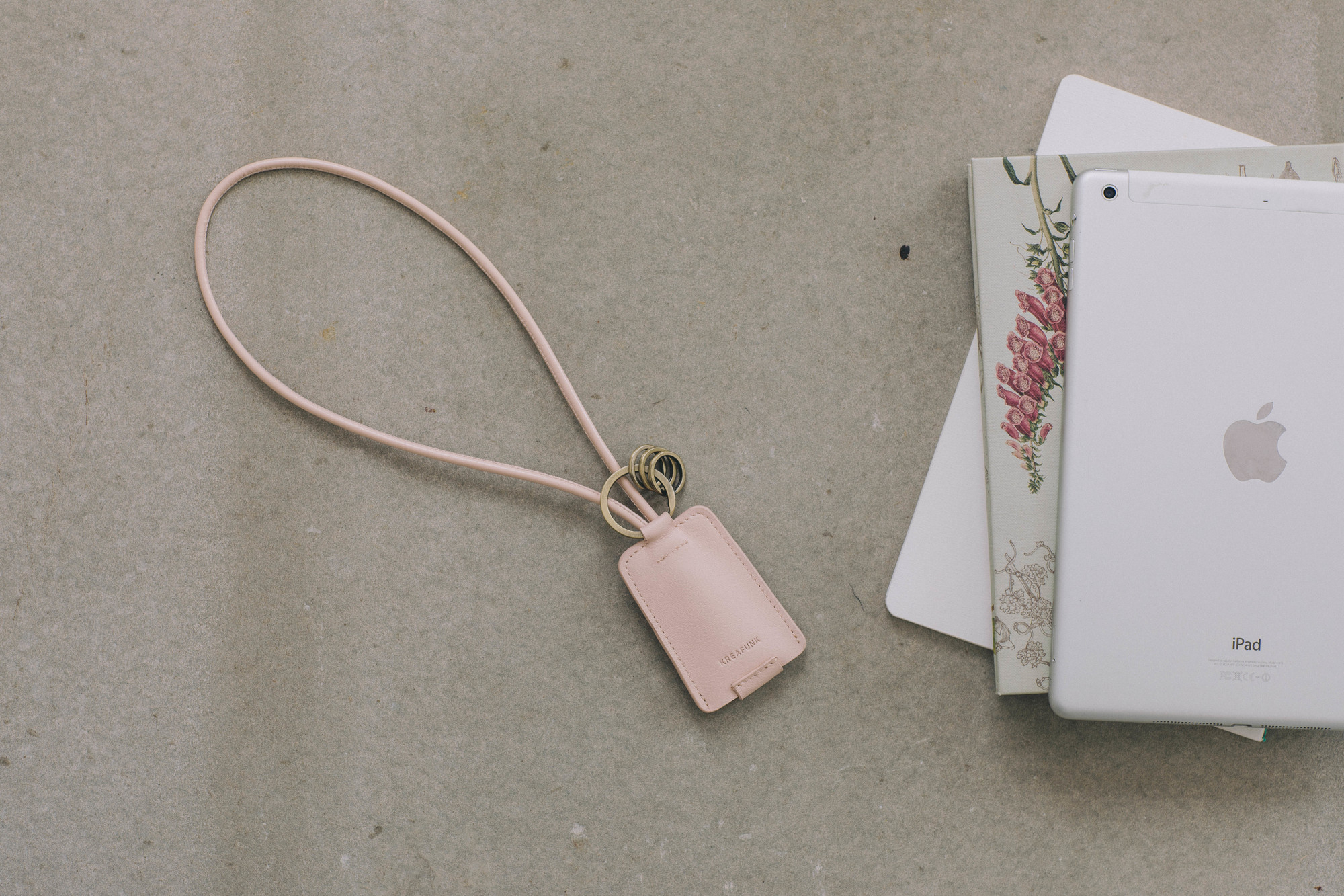 Nahaufnahme des Kreafunk cCHAIN Schlüsselanhängers in Rosa mit USB-Kabel, neben einem iPad.