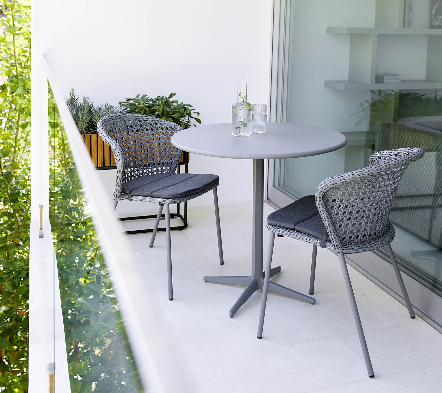 Graue Lean Stühle von Cane-Line mit Rattan-Geflecht und passendem Tisch auf einem Balkon.