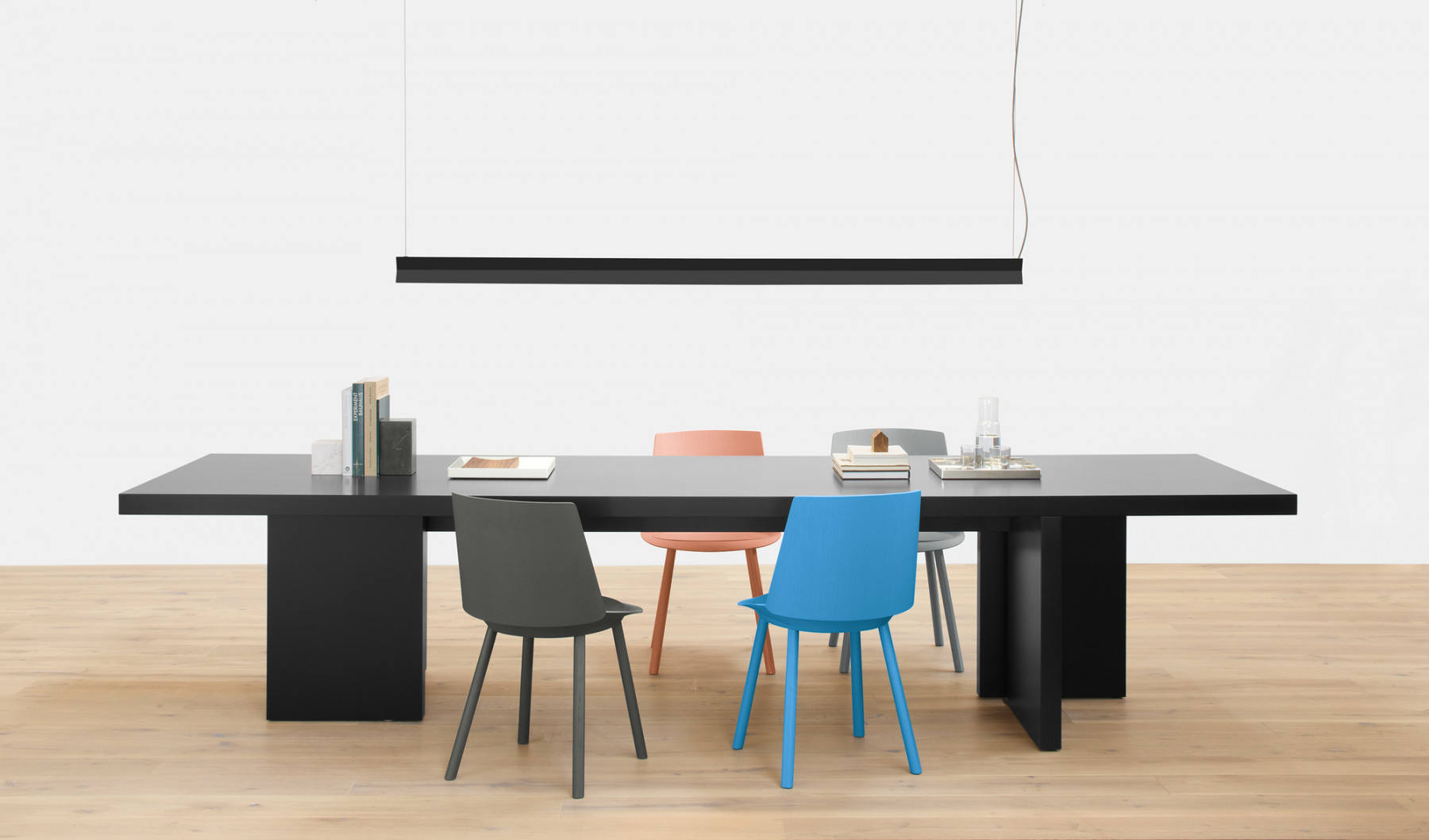 Schwarzer Esstisch mit farbigen Stühlen und moderner Pendelleuchte, ideal für Esszimmer und Konferenzraum.
