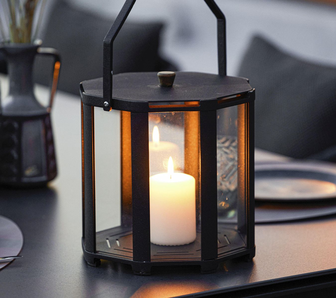 Nahaufnahme der Cane-Line Lightlux Laterne, groß, aus Teakholz, mit brennender Kerze auf einem Tisch.