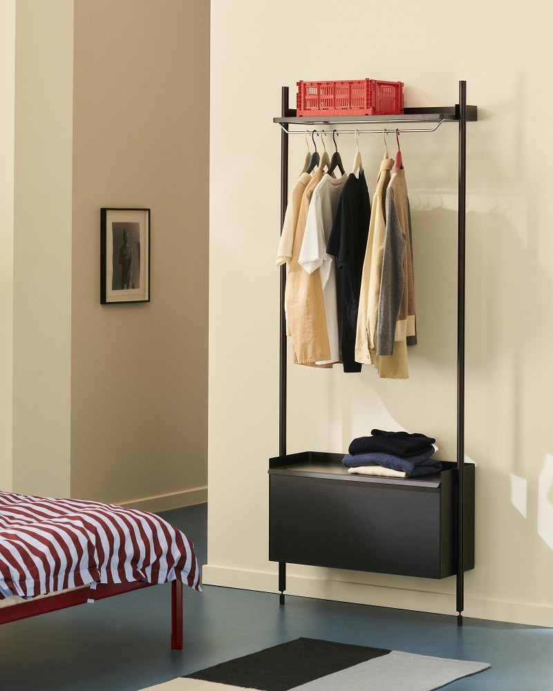 Schlafzimmer-Szene mit Hay Connect Bett im Vordergrund und minimalistischem Kleiderständer mit Kleidung und Aufbewahrungsbox.