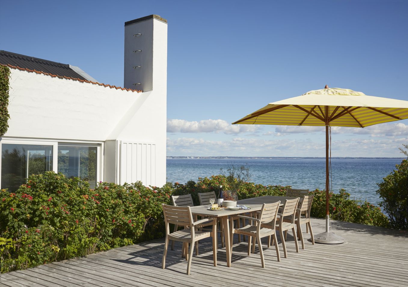 Ballare Chair Stuhl von Skagerak by Fritz Hansen: Gartentisch mit Stühlen und Sonnenschirm auf Holzterrasse am Meer.