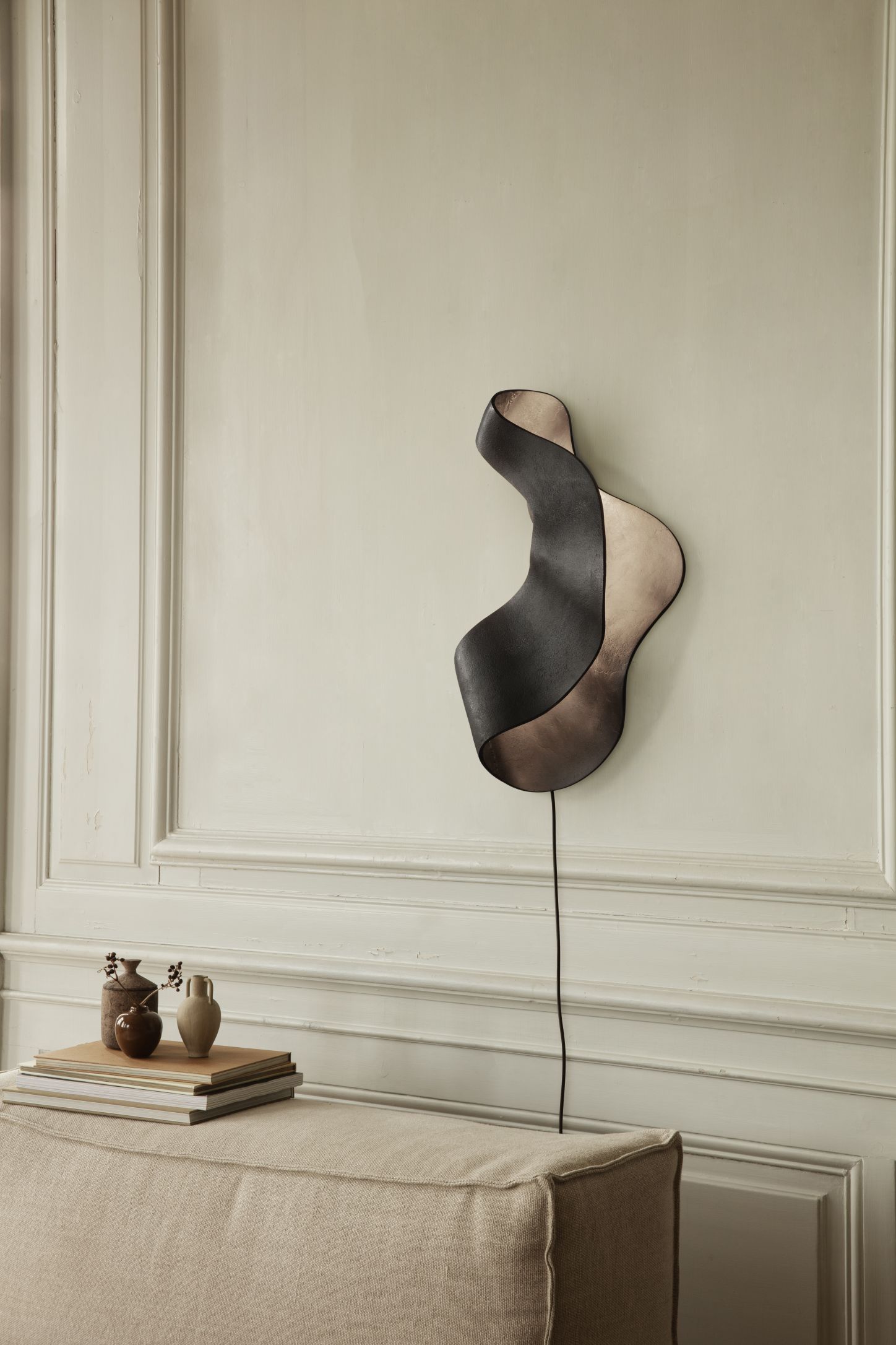 Oyster Wandleuchte von Ferm Living, abstraktes Design in Schwarz und Beige an einer Wand.
