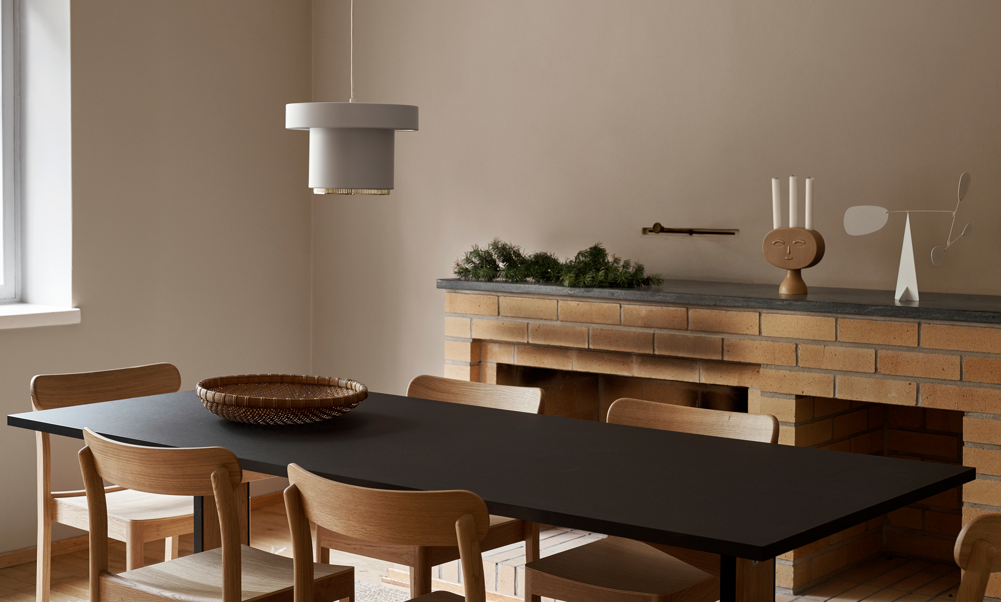 A201 Pendelleuchte von Artek über Esstisch mit Holzstühlen und Kamin im Hintergrund.