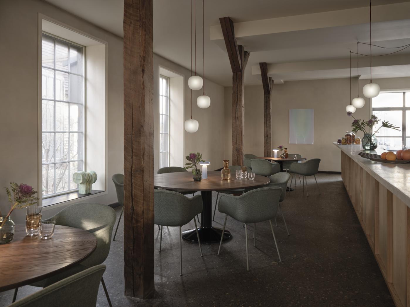 MIDST Table Esstisch von Muuto in einem Restaurant mit Holzsäulen und Pendelleuchten.