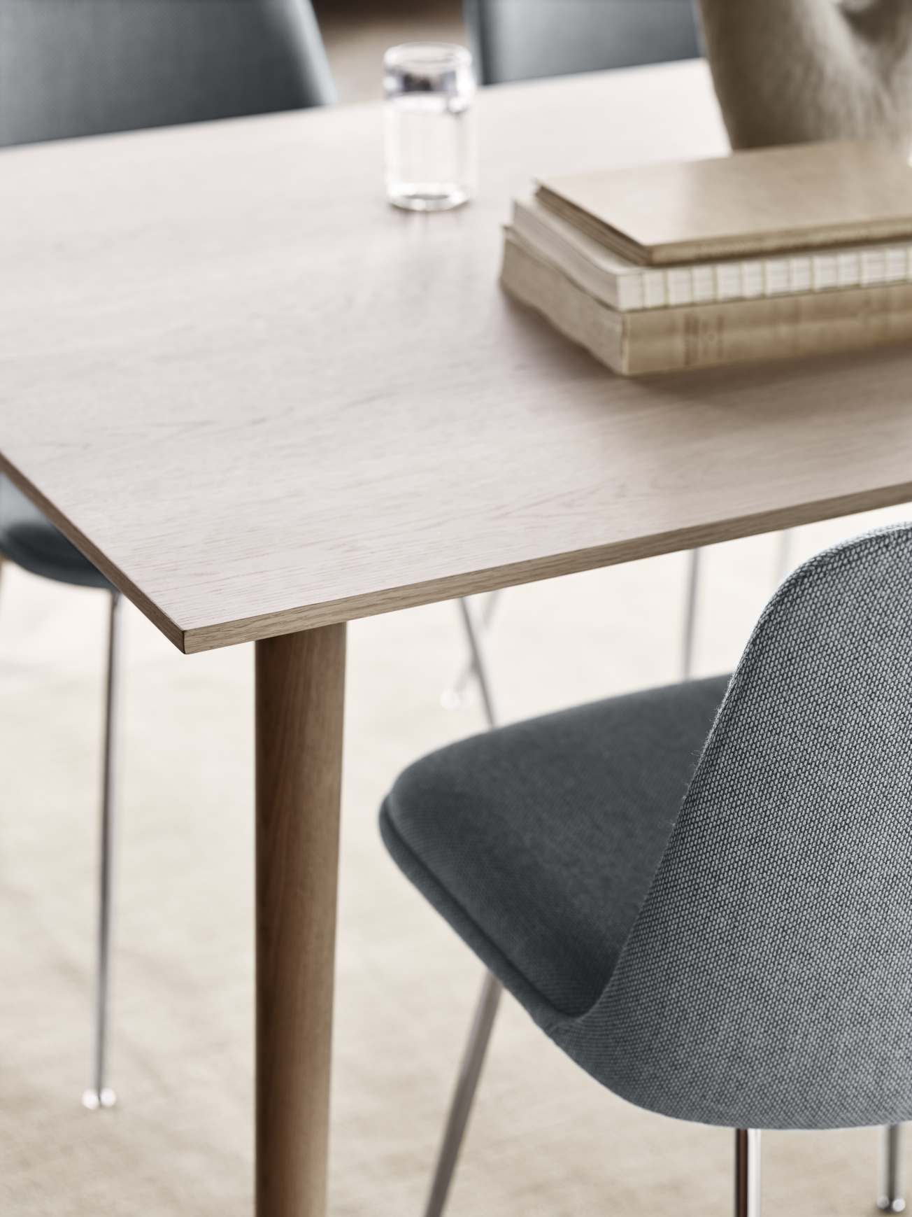 Detailaufnahme des AndTradition In Between Tisches SK5/SK6 aus Eiche mit Stuhl, Büchern und Wasserglas.