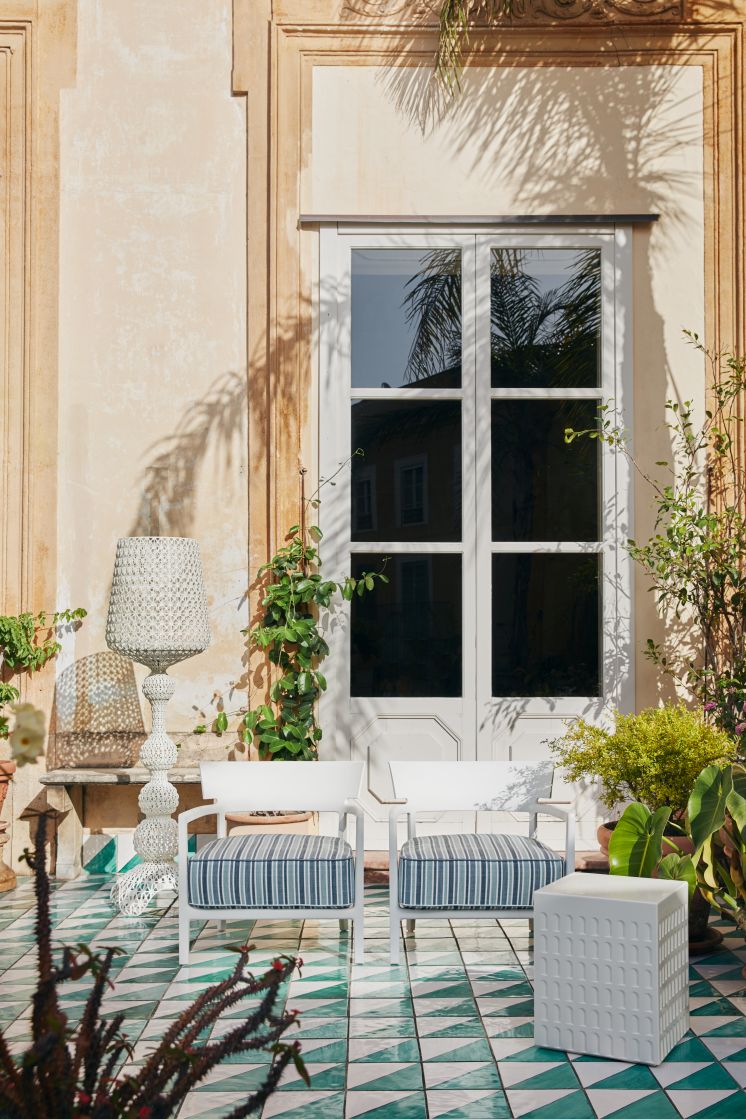 Zwei weiße Kartell Outdoor Sessel "Cara" mit gestreiften Kissen auf einer sonnigen Terrasse.