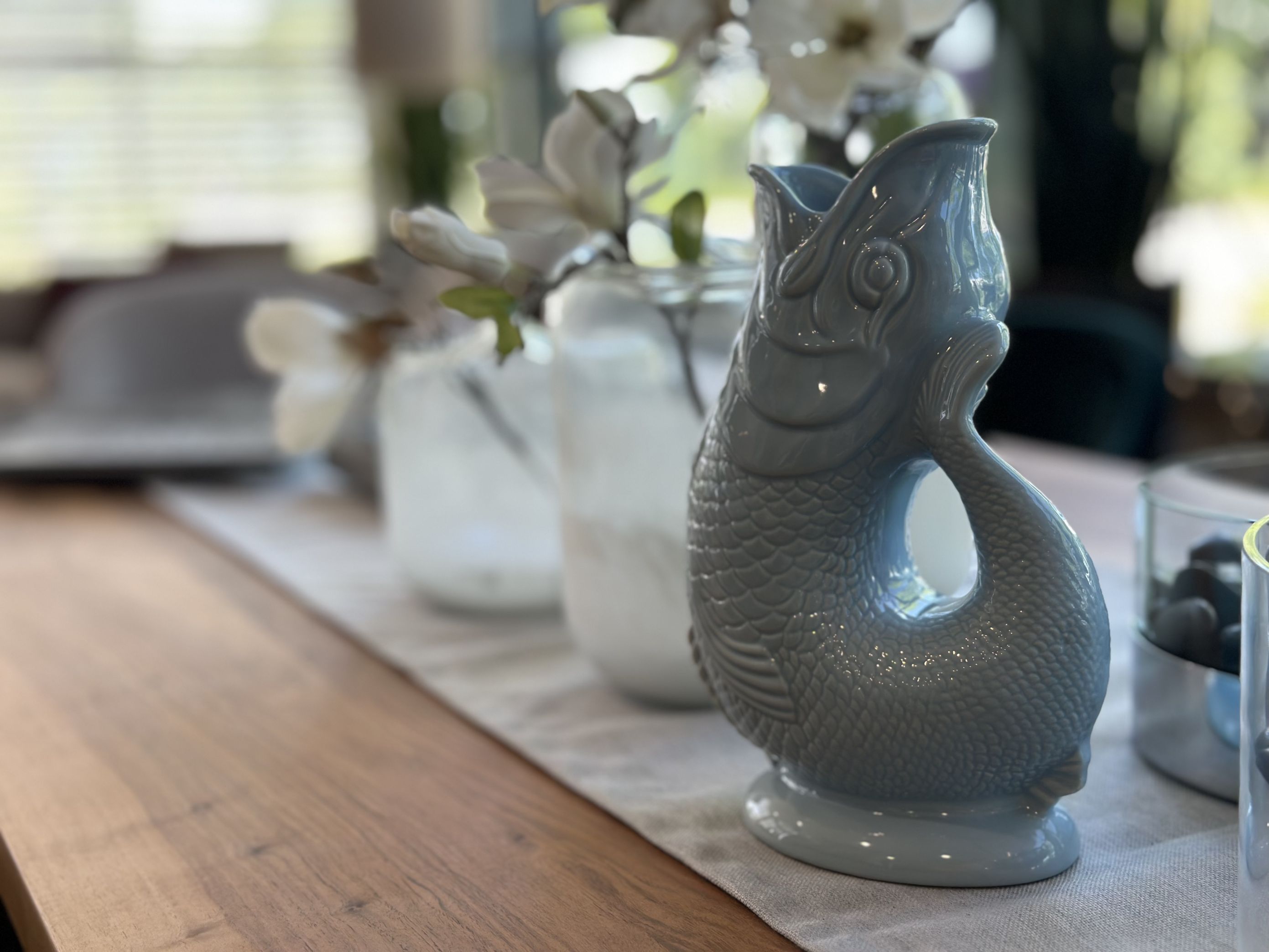 Helle Gluckigluck Karaffe in Fischform, hellblau, XL, als Vase auf einem Tisch.