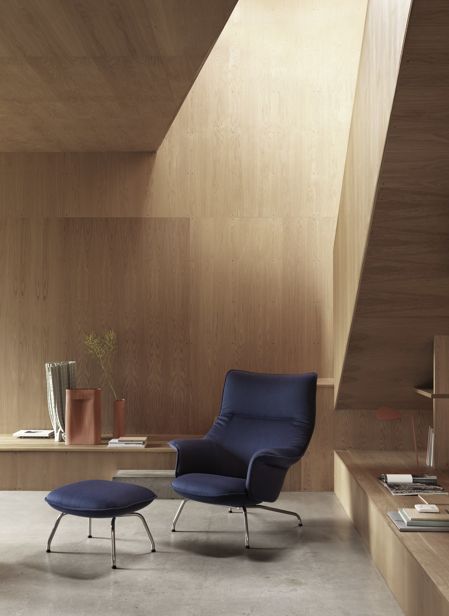 Blauer Muuto Doze Ottoman mit passendem Sessel in modernem, hellem Raum mit Holzverkleidung.