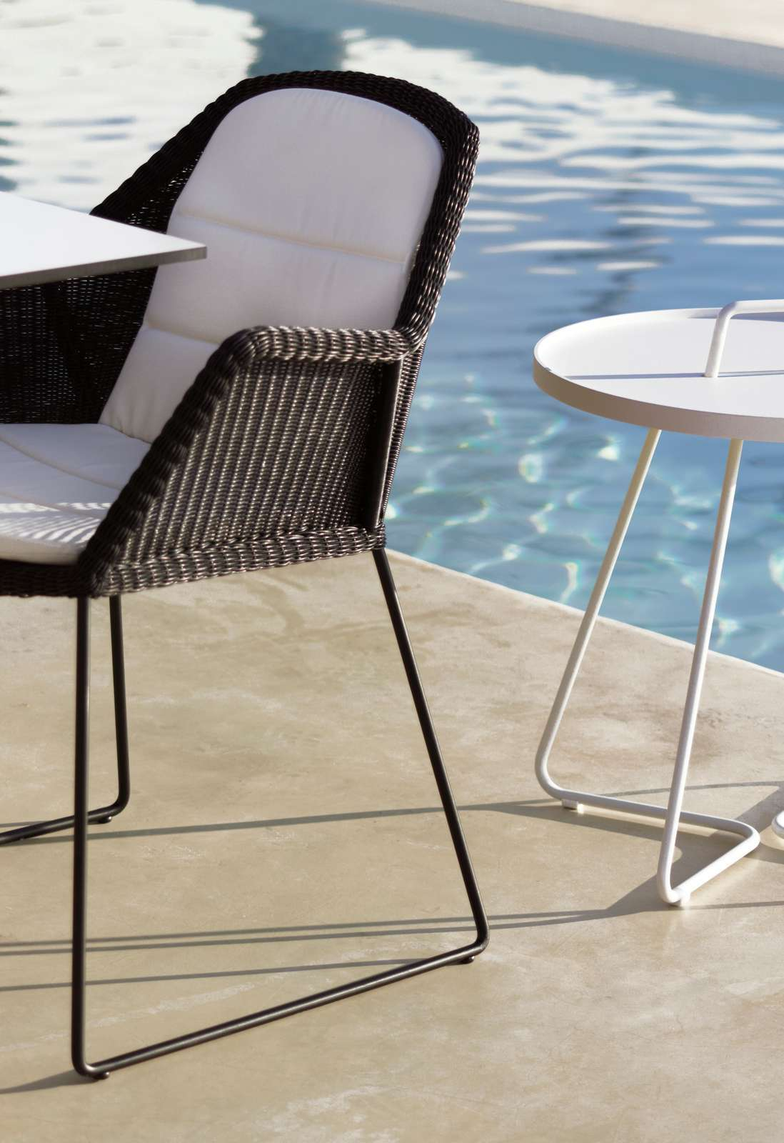 Breeze Outdoor Stuhl mit Kufengestell von Cane-Line, schwarzes Rattan mit weißen Polstern am Pool.