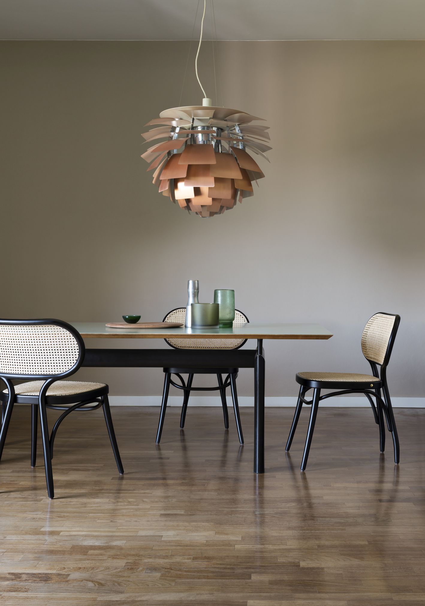 Esszimmer mit modernem Esstisch, Rattan Stühlen und Designer-Hängeleuchte in Kupferoptik.