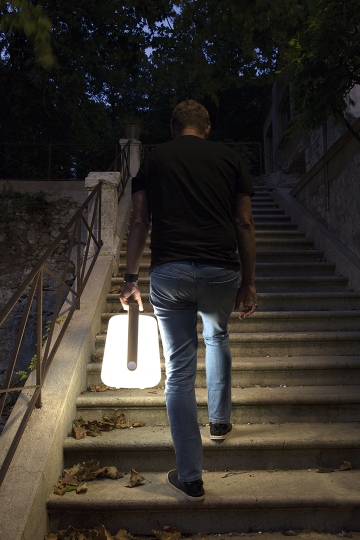 Mann trägt Balad Bamboo Tischleuchte von Fermob eine Treppe hinauf, warmes Licht beleuchtet die Stufen.