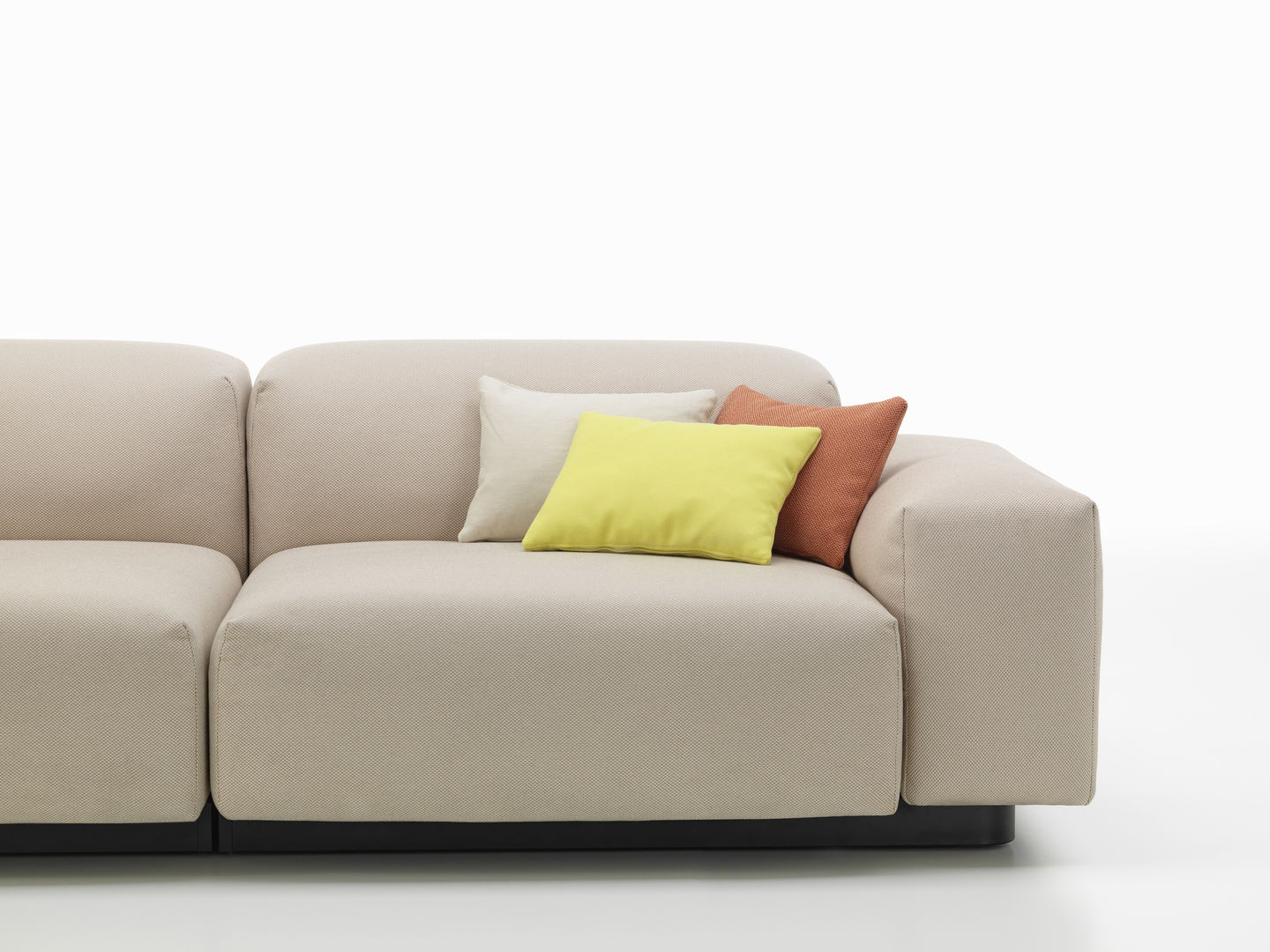 Beige Couch mit drei dekorativen Vitra Kissen in Gelb, Weiß und Orange auf der Armlehne.