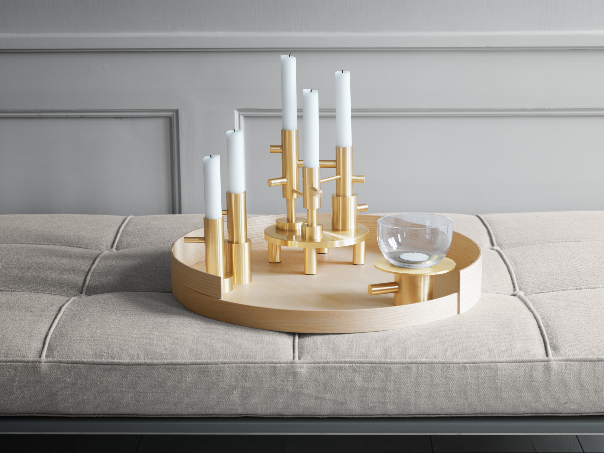 Goldener Fritz Hansen Kerzenhalter mit weißen Kerzen auf Holztablett, dekorative Wohnaccessoires.