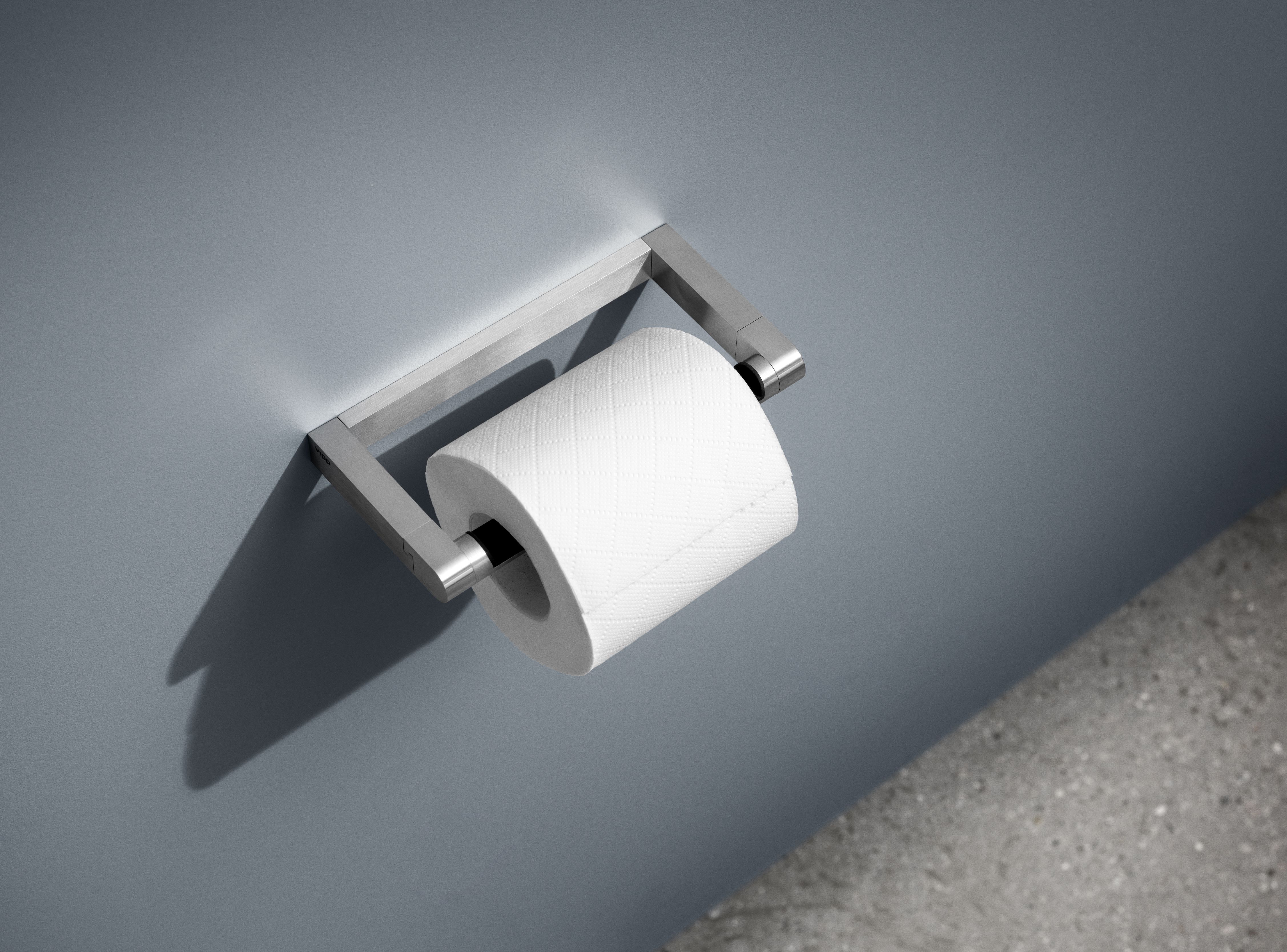 Vipp WC-Rollenhalter aus gebürstetem Edelstahl mit einer weißen Toilettenpapierrolle an grauer Wand.