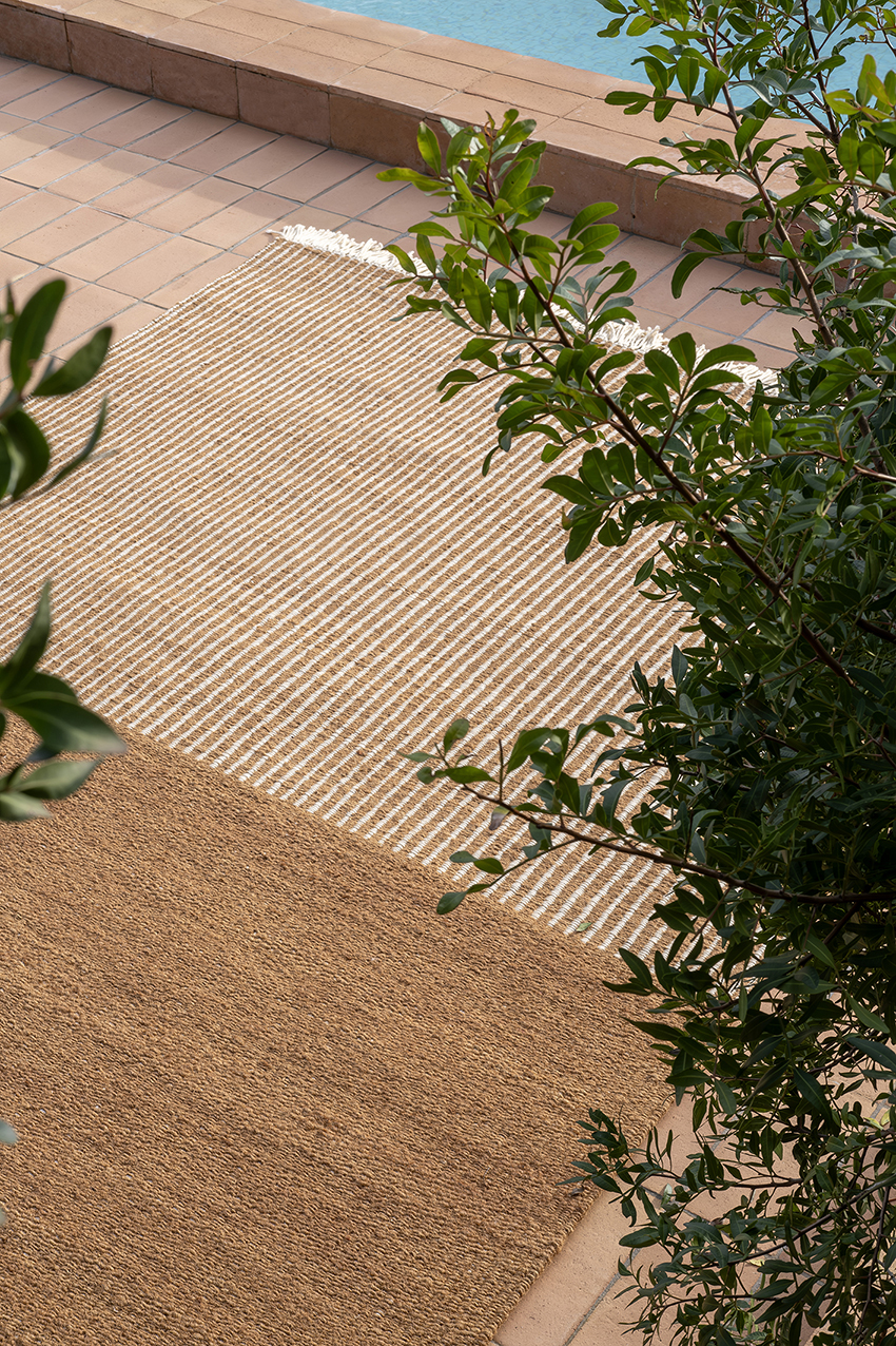 Nanimarquina Garden Outdoor Teppich, braun und beige gestreift, auf einer Terrasse neben einem Pool.