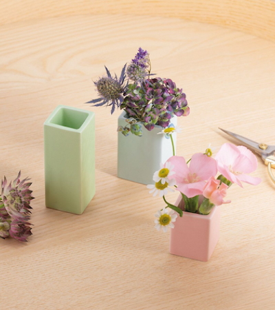 Drei kleine, pastellfarbene Vasen mit Blumen auf einem Holztisch, Dekoration für Zuhause.