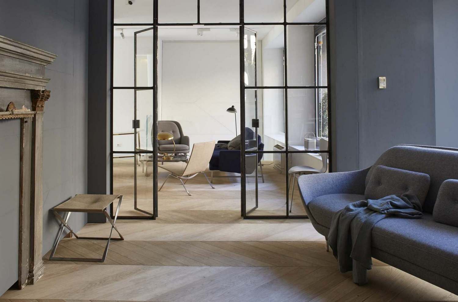 Grauer Fri Sessel von Fritz Hansen in modernem Wohnzimmer mit Glaswand und Parkettboden.