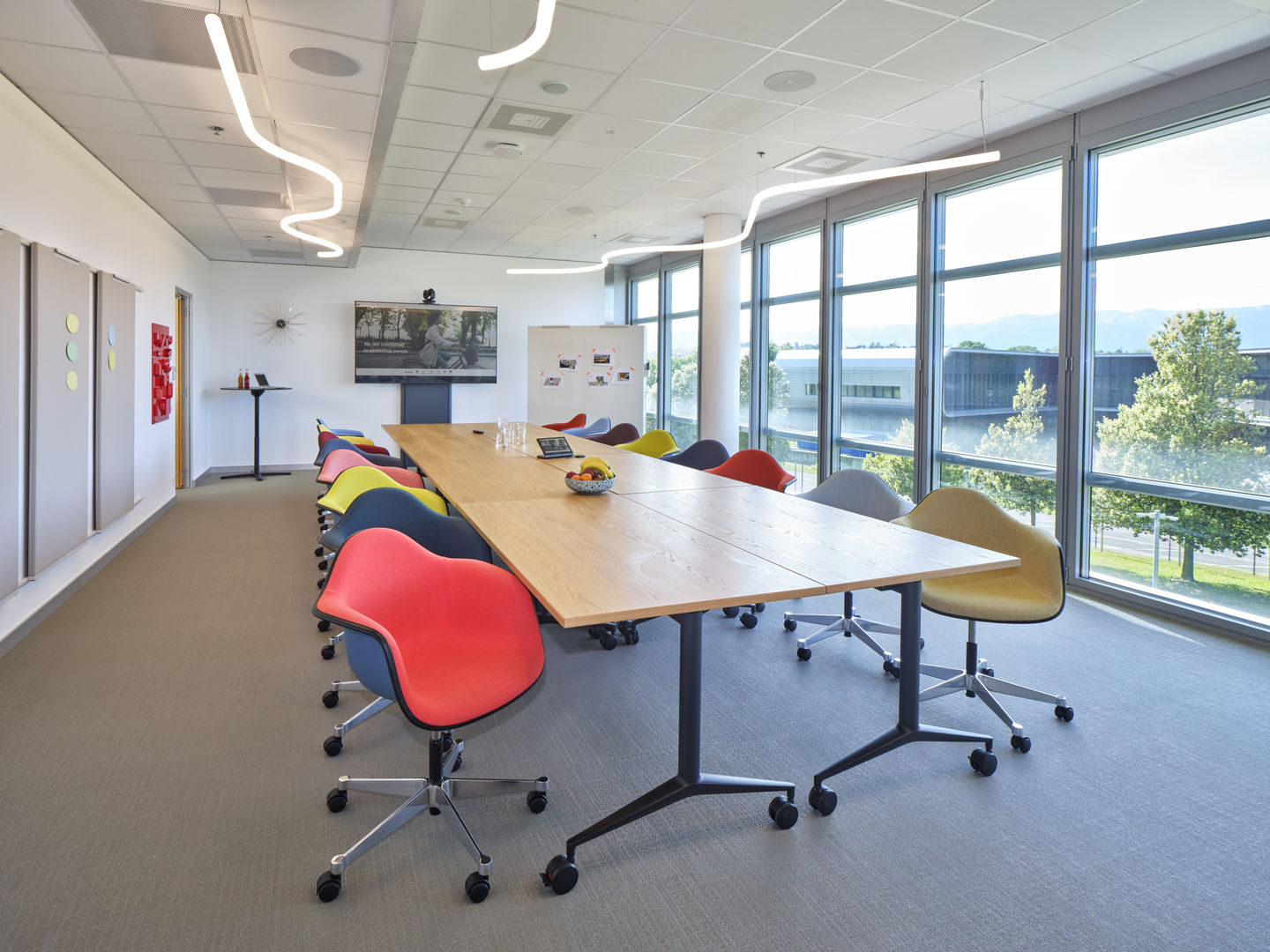 Konferenzraum mit langem Vitra Klapptisch MedaMorph und bunten Bürostühlen an großen Fenstern.