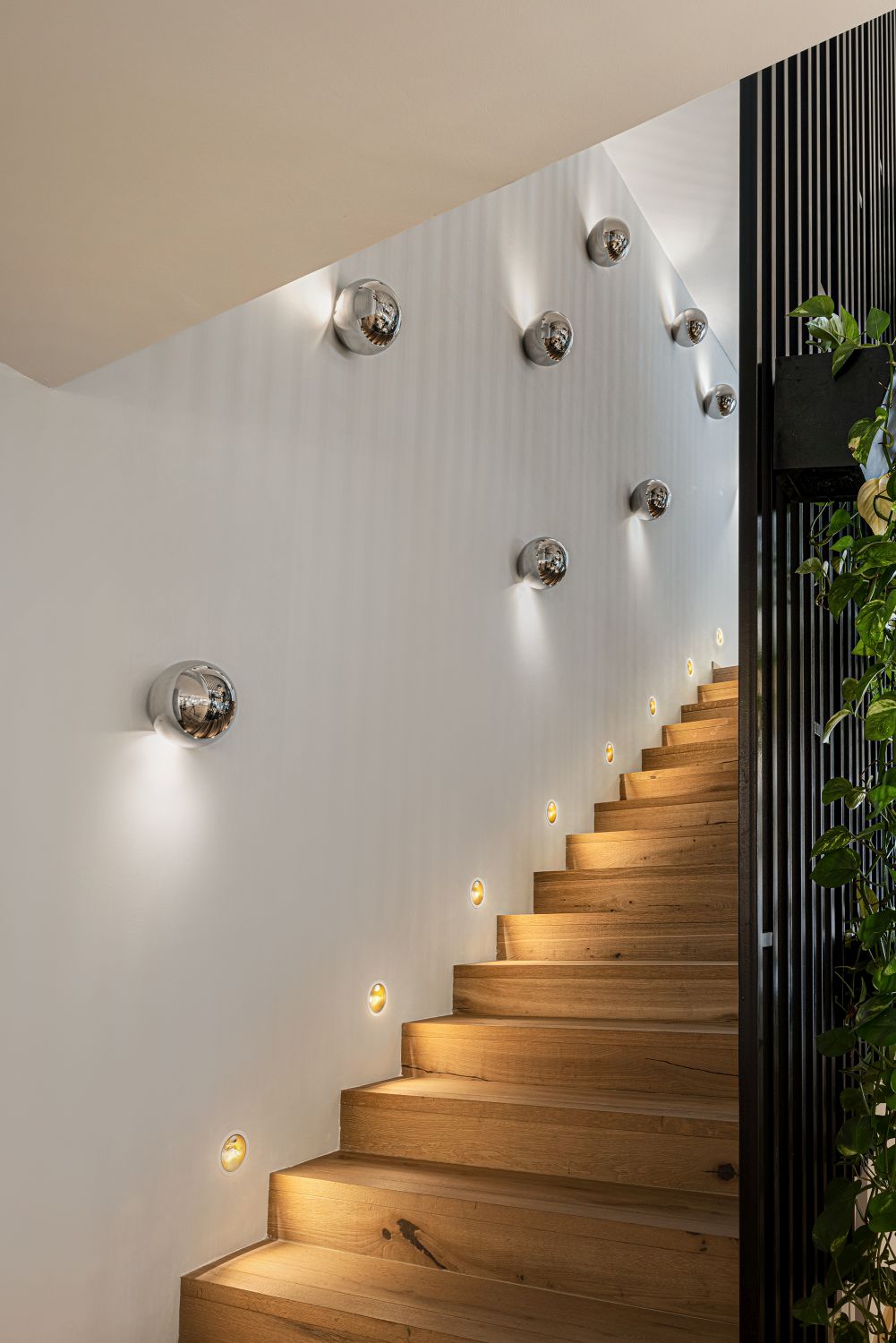 Sfera Wandleuchten von Catellani & Smith beleuchten ein Treppenhaus mit Holzstufen und indirektem Licht.