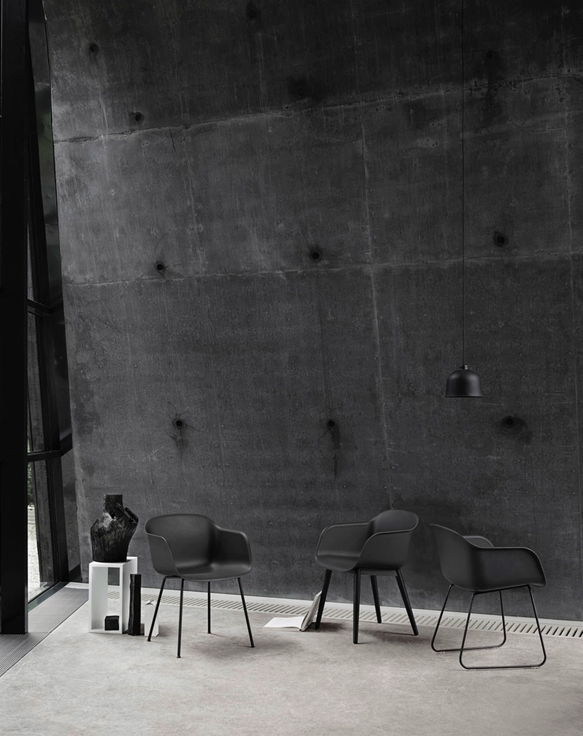 Drei schwarze Fiber Armchair Stühle von Muuto mit unterschiedlichen Gestellen vor Betonwand.