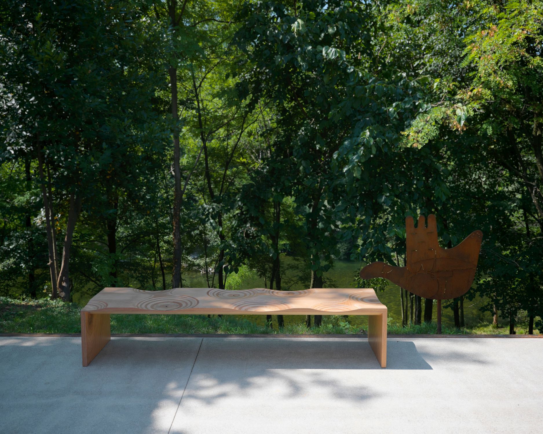 Casamania Horm Ripples Outdoor Bank aus Holz vor grüner Naturkulisse für Garten und Terrasse.