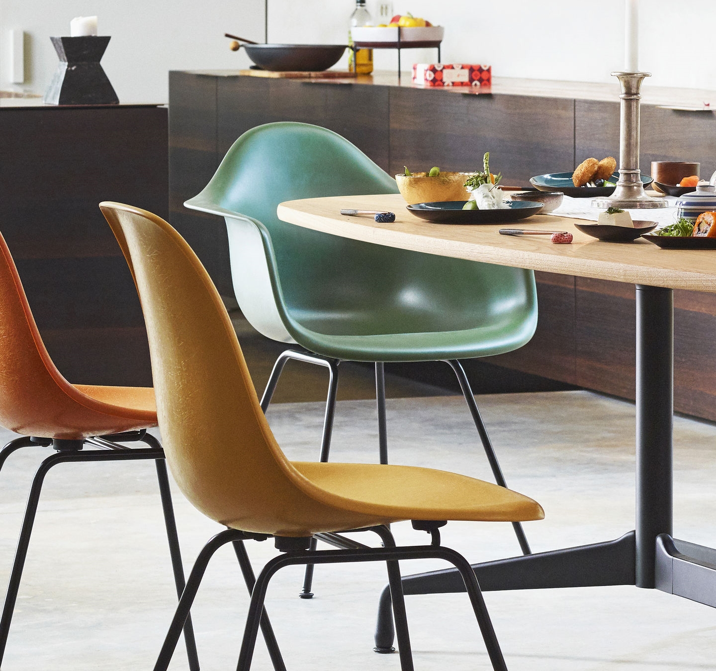 Drei farbige Kunststoffstühle mit schwarzem Metallgestell am Esstisch, modernes Möbeldesign für Esszimmer und Küche.