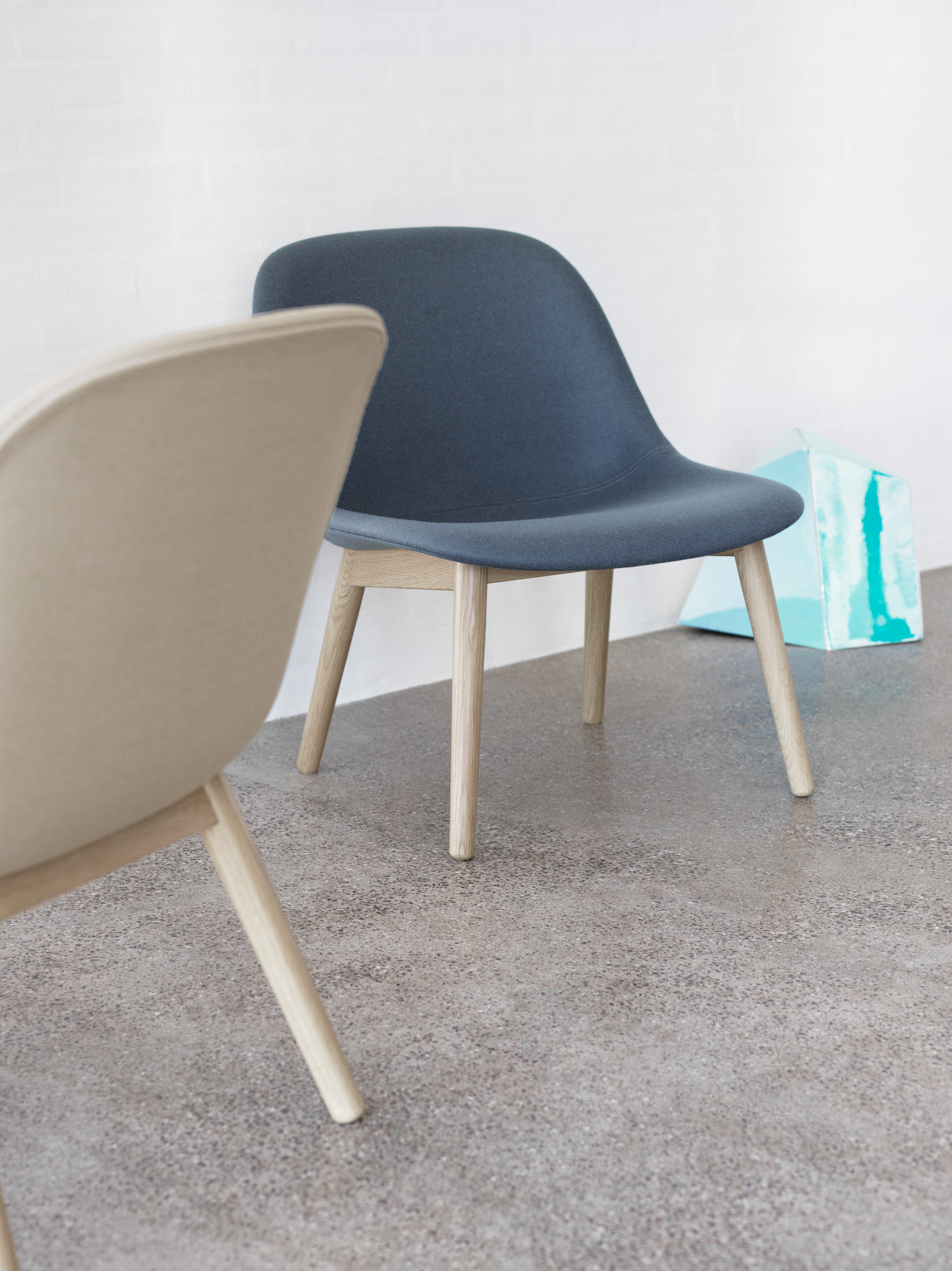 Muuto Fiber Lounge Chair mit Holzgestell in Blau und Beige vor weißer Wand.